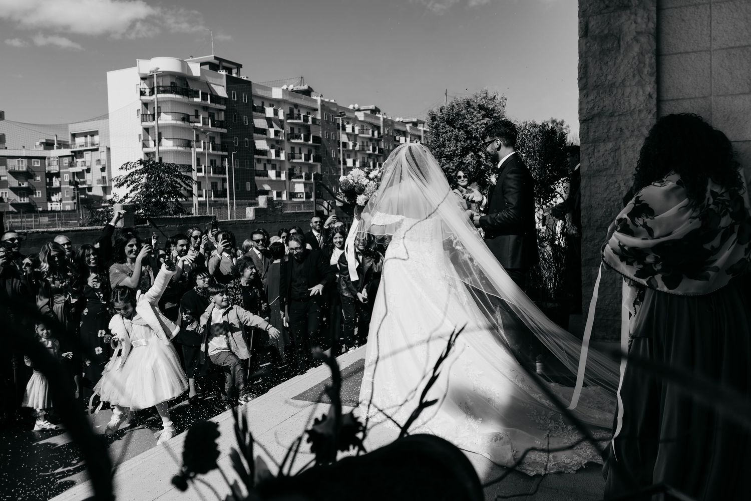 Black and white photo of a bride in a veil and gown exiting a church surrounded by a large crowd.