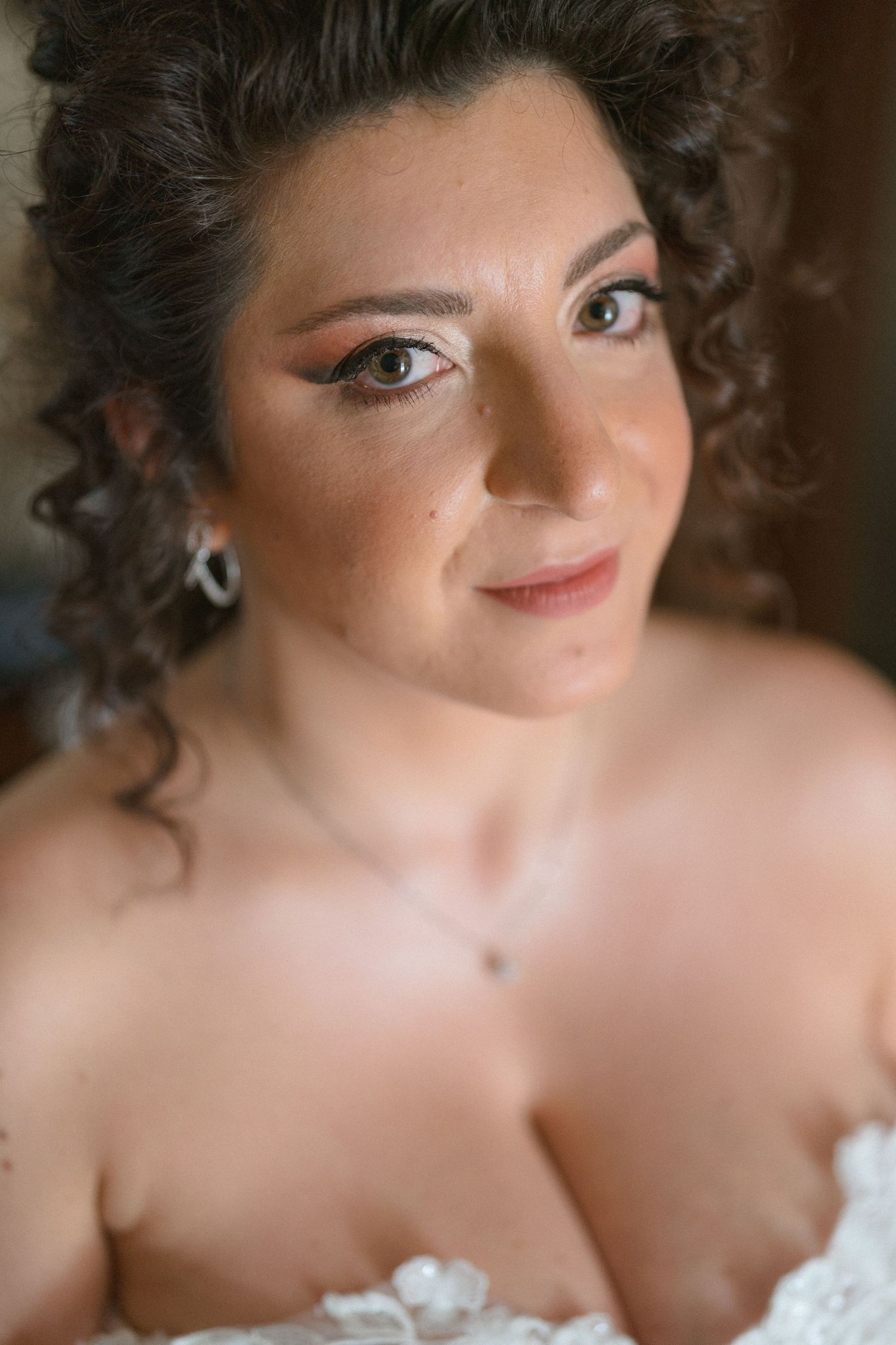 Close-up portrait of a beautiful bride with curly hair, elegant makeup, and delicate jewelry on her wedding day.