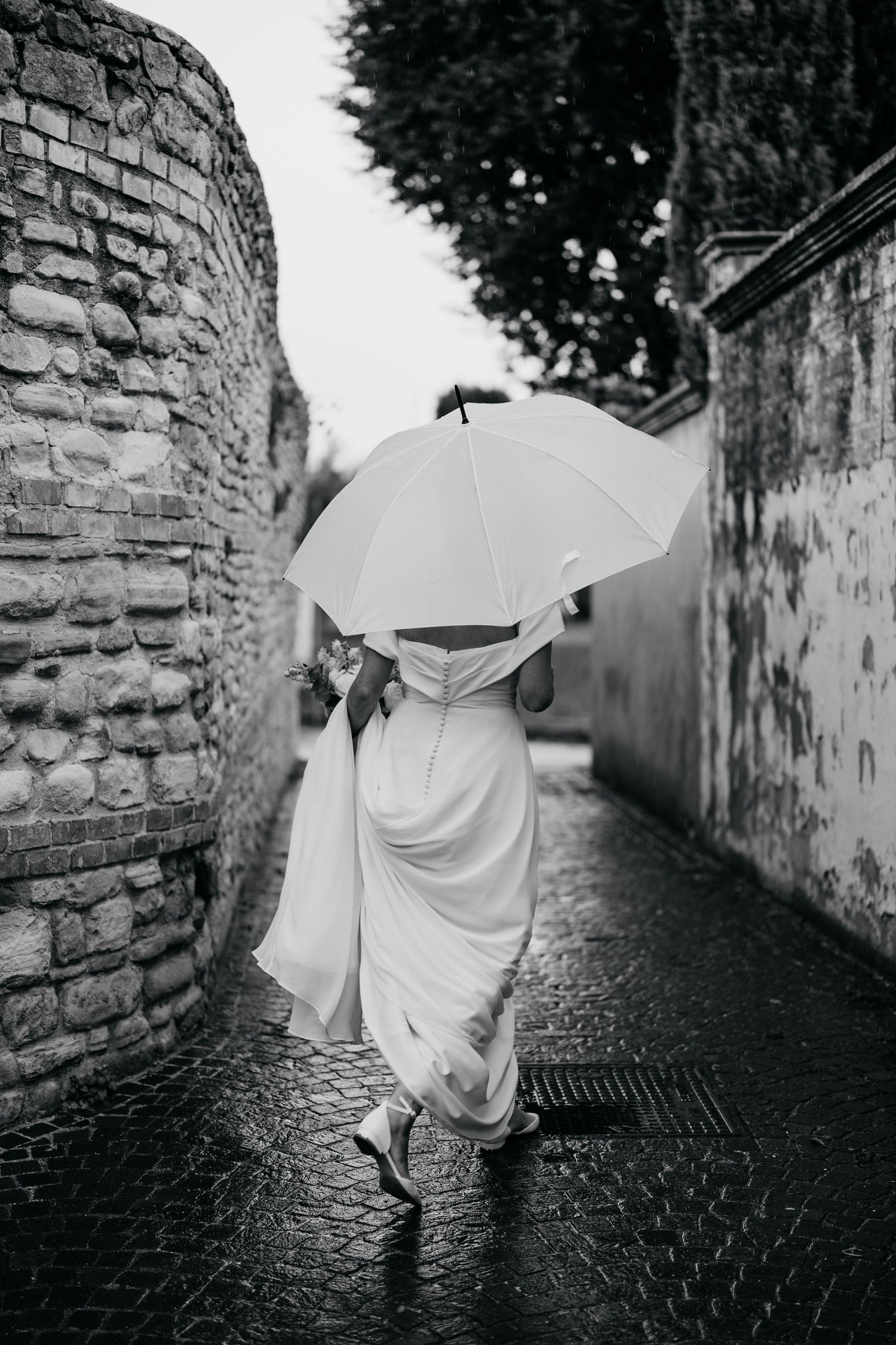 Black and white photos of flowing white dress moving down a cobblestone alley with stone walls.