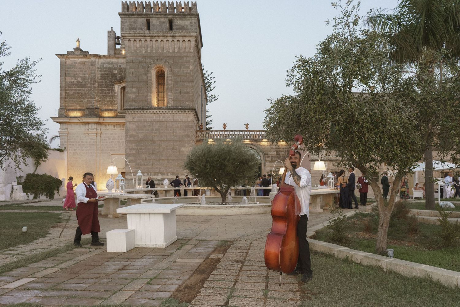 A musician plays double bass outside a historic stone tower during an event.