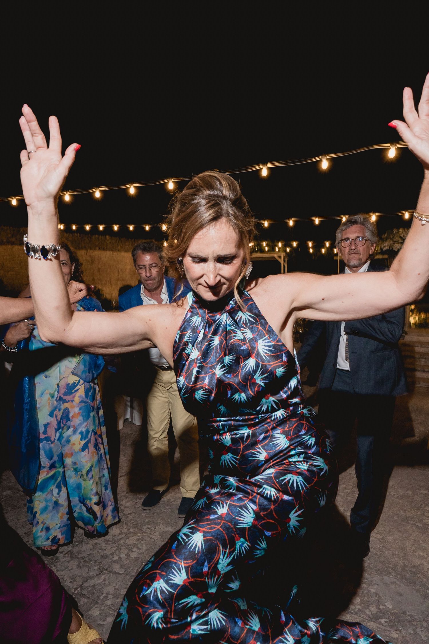 Wedding guest dancing energetically under string lights in a floral pattern dress.