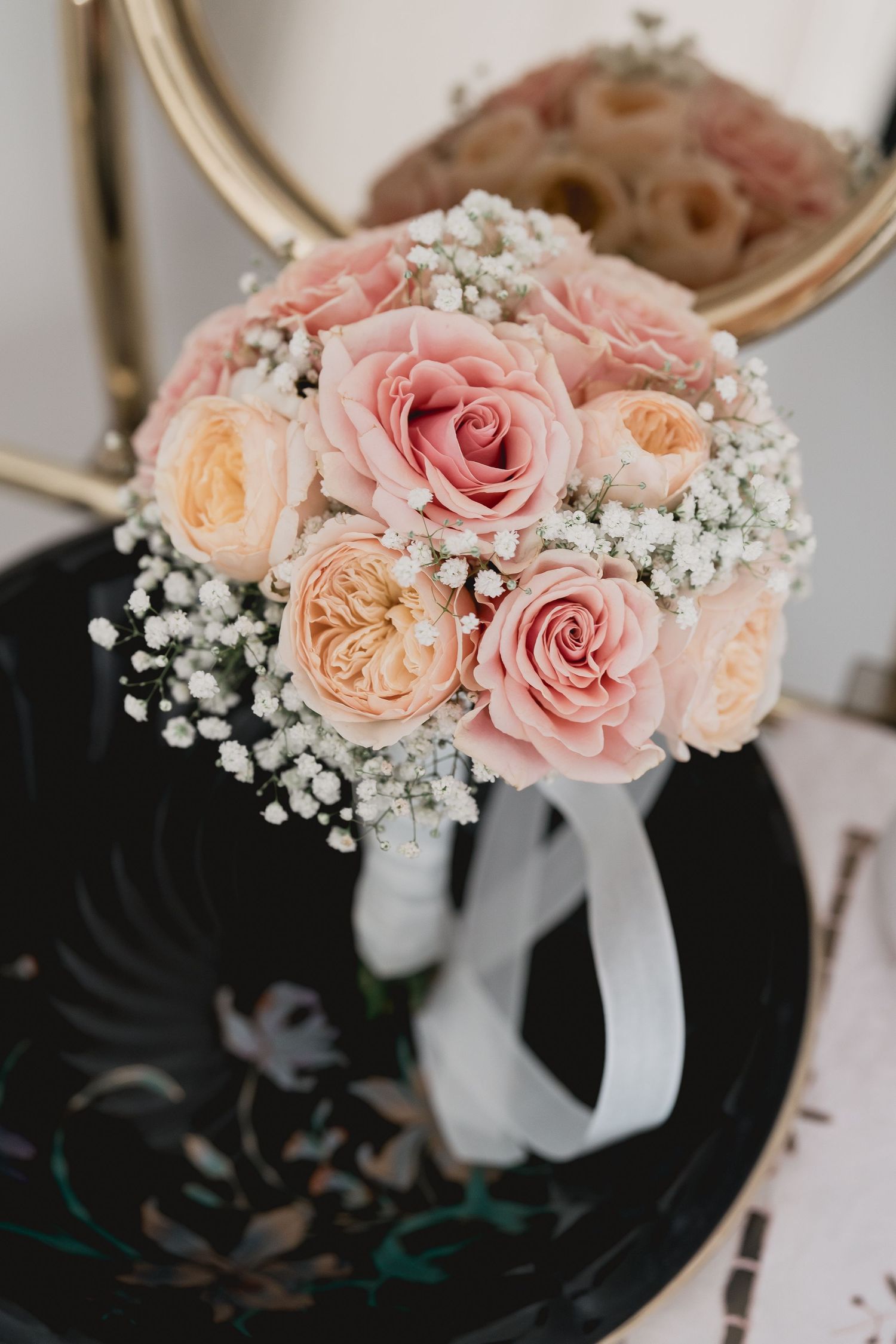 Romantic bouquet of pink and peach roses with baby's breath against dark background.