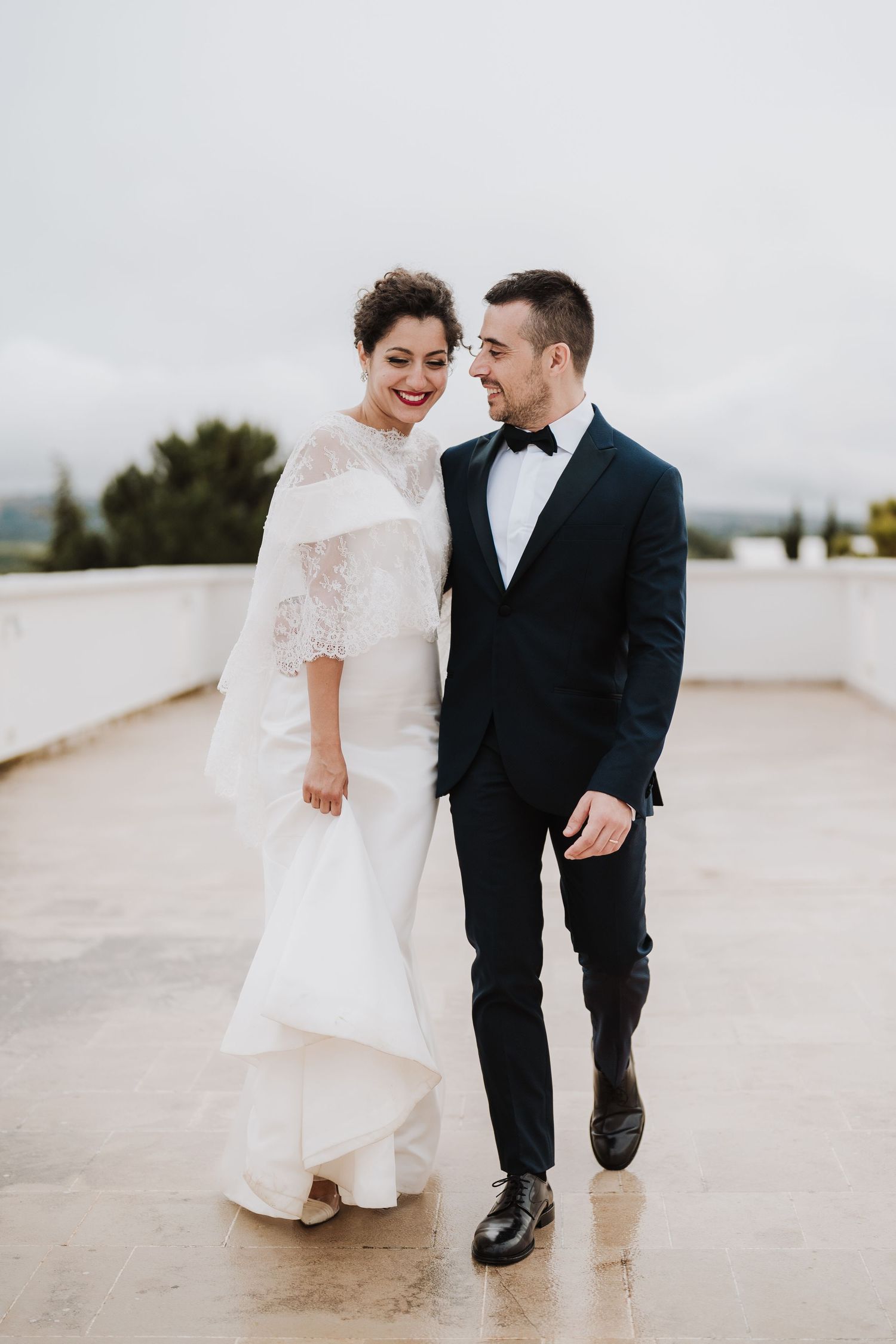 Romantic wedding portrait on a rooftop terrace with cloudy sky backdrop.