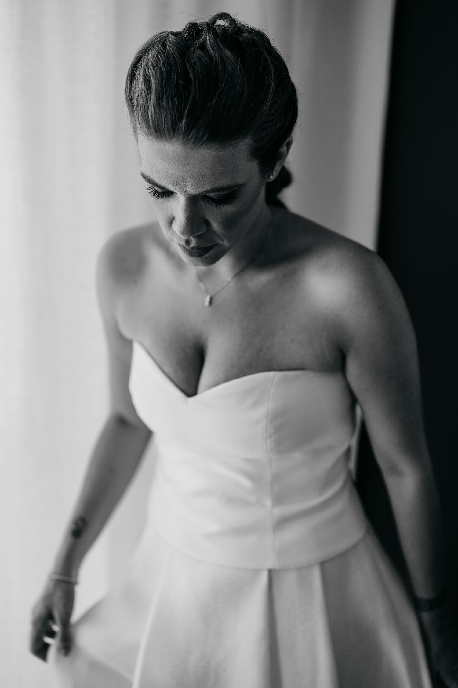 A dramatic black and white portrait of someone wearing a strapless white formal dress.