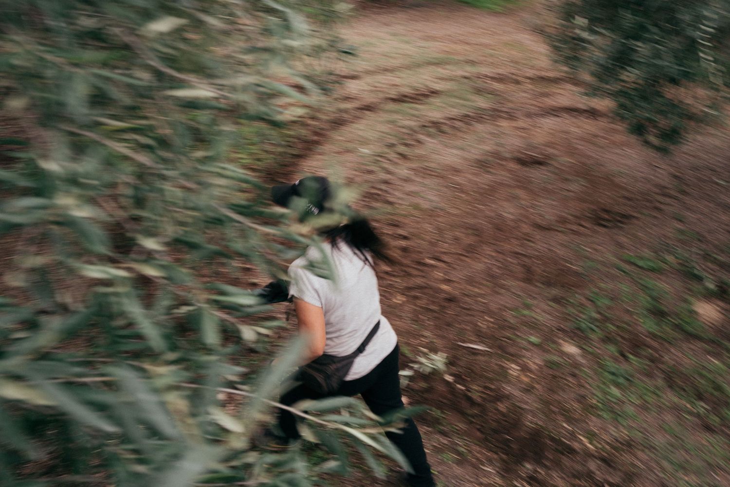 A person in casual wear walks along a winding dirt trail surrounded by green foliage captured in motion blur.