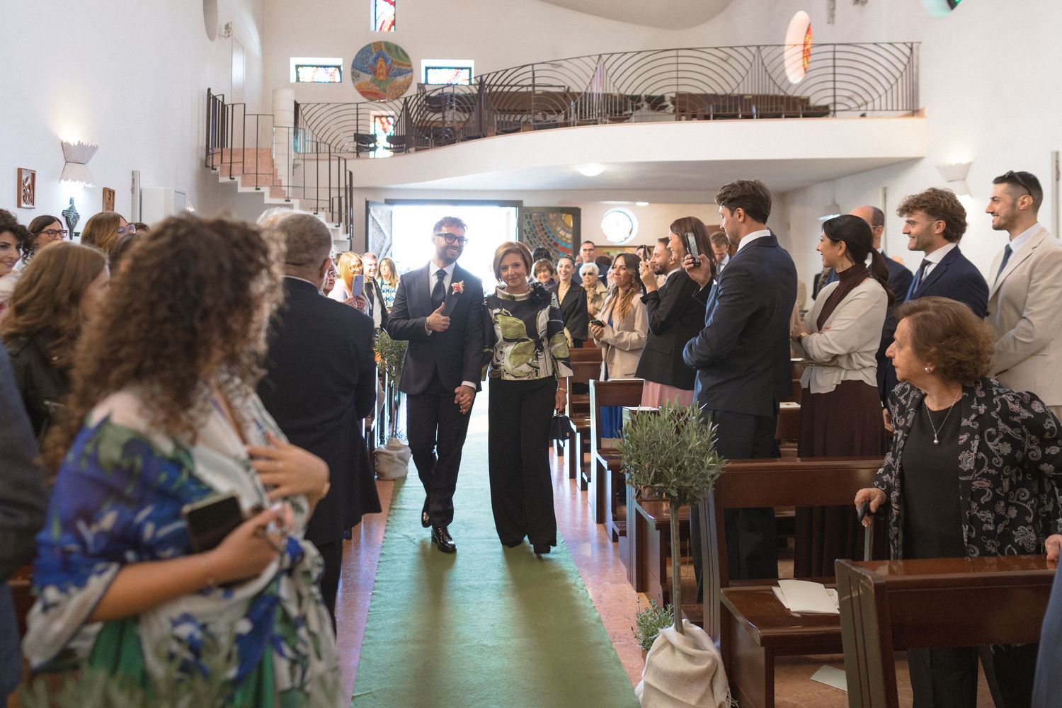 Guests stand in church aisle as bride walks toward altar during wedding ceremony.
