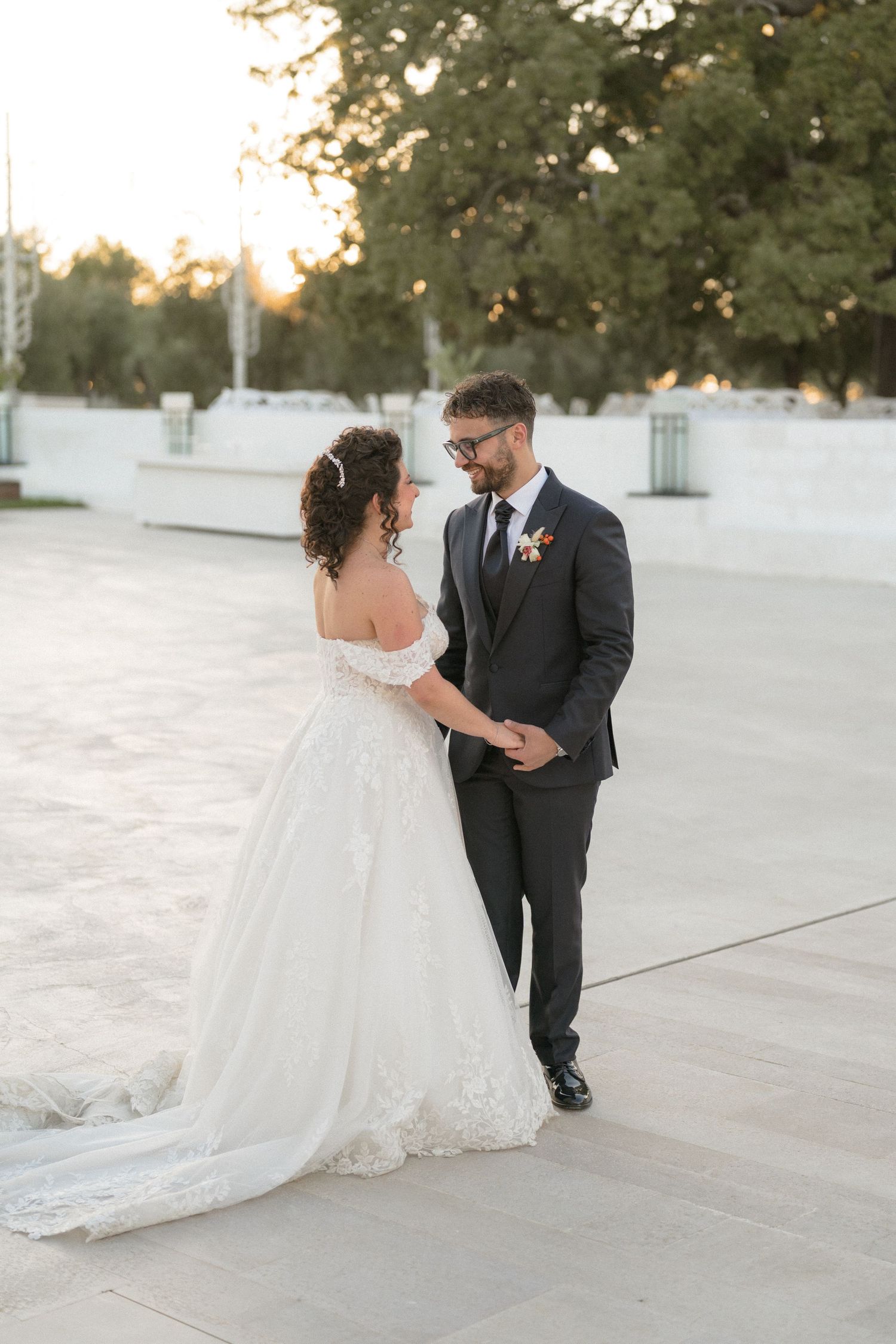 Bride and groom hold hands and gaze at each other at sunset on their wedding day.