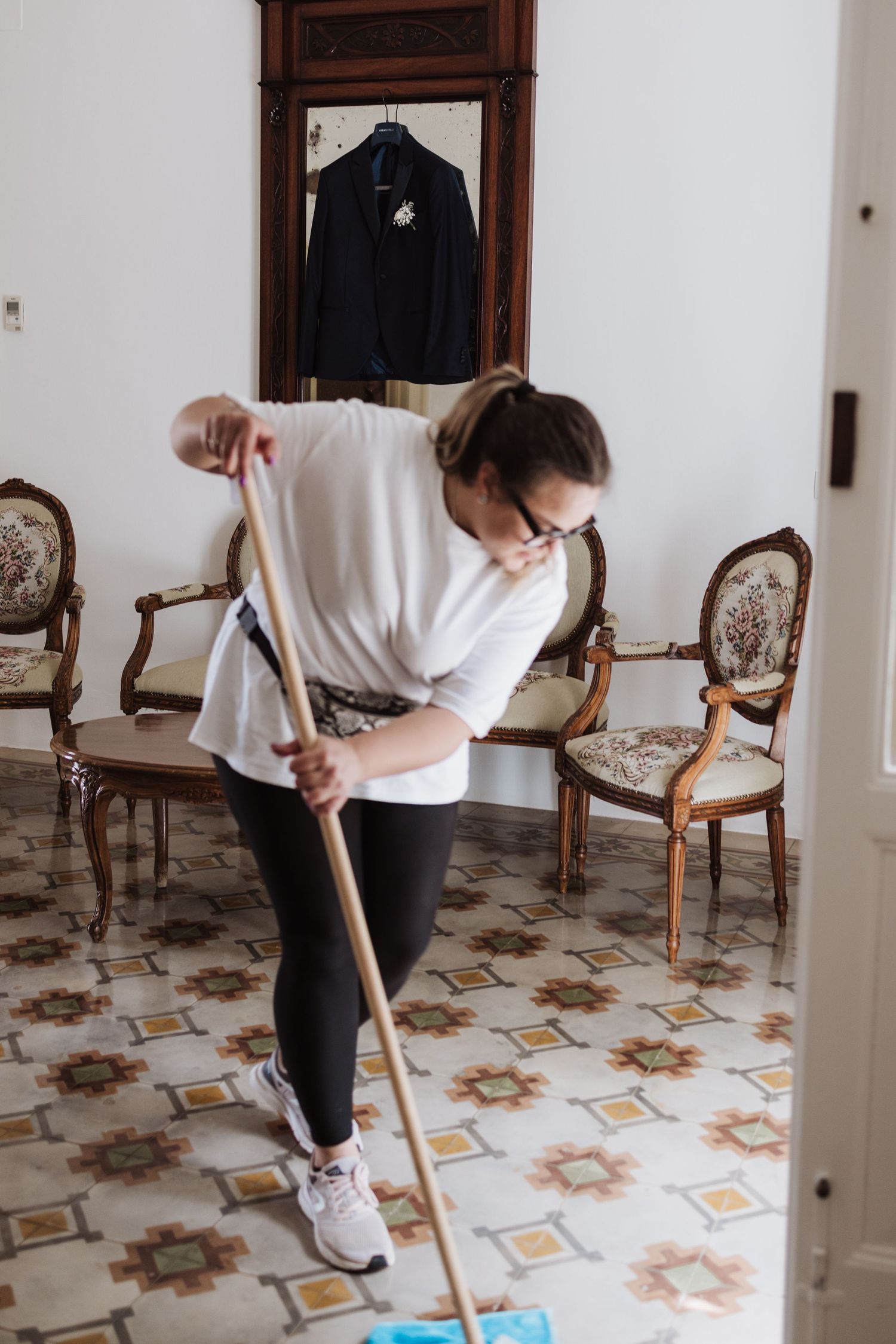 Person mopping decorative tiled floor in a room with antique chairs.