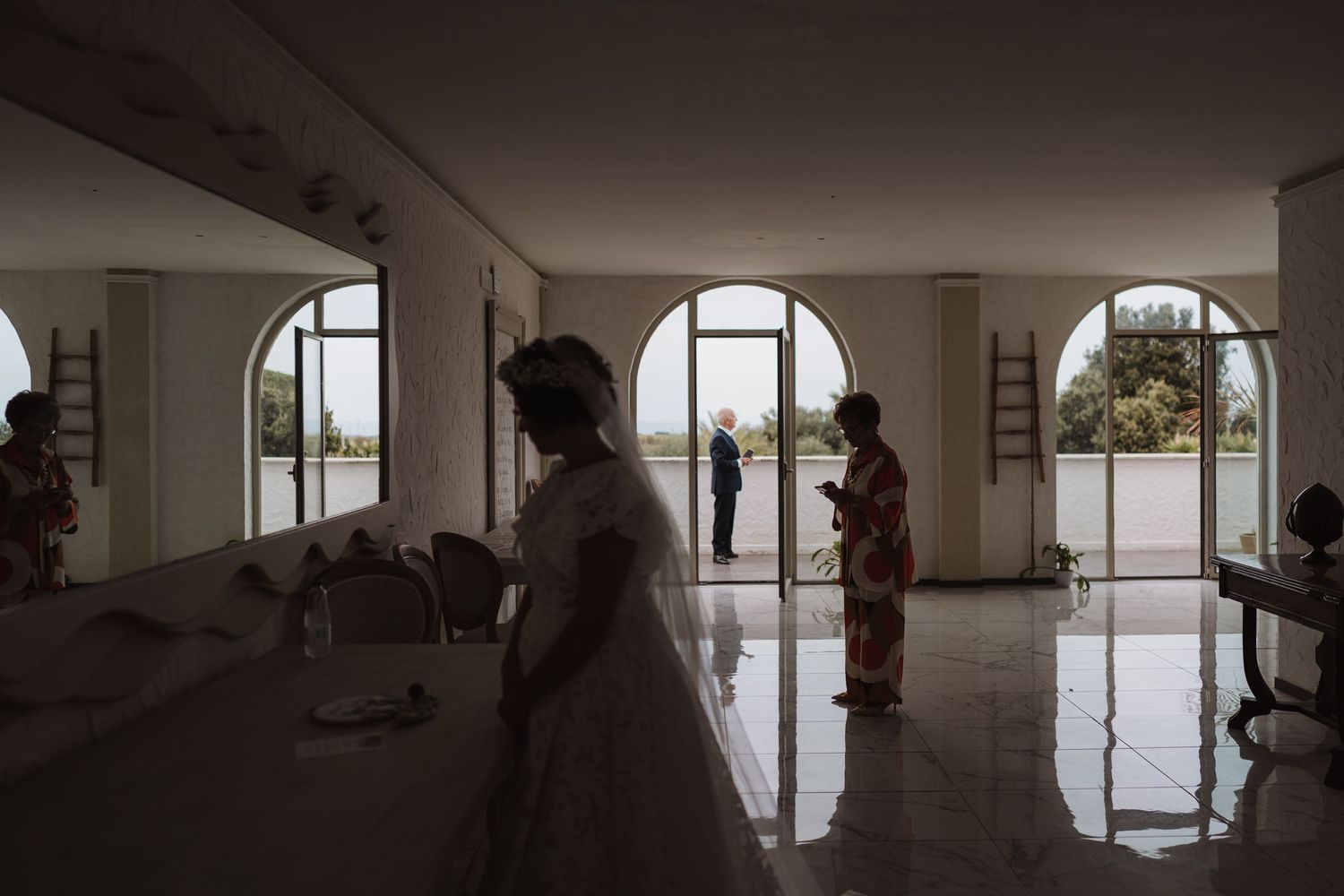 Interior of an elegant venue with arched windows and people preparing for a wedding ceremony.