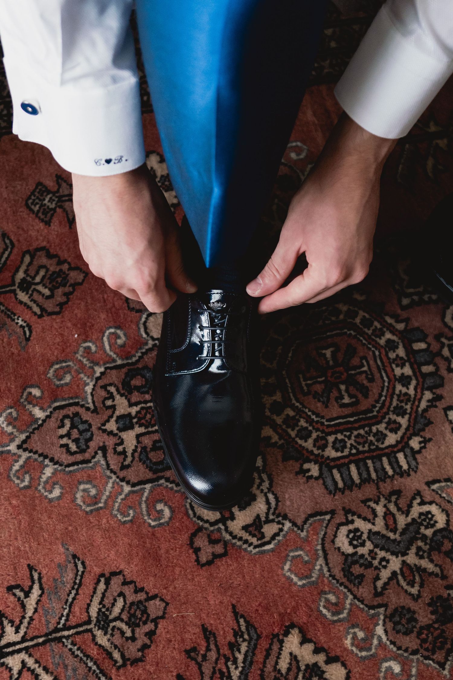Wedding preparation showing dress shoes being laced on ornate oriental carpet.