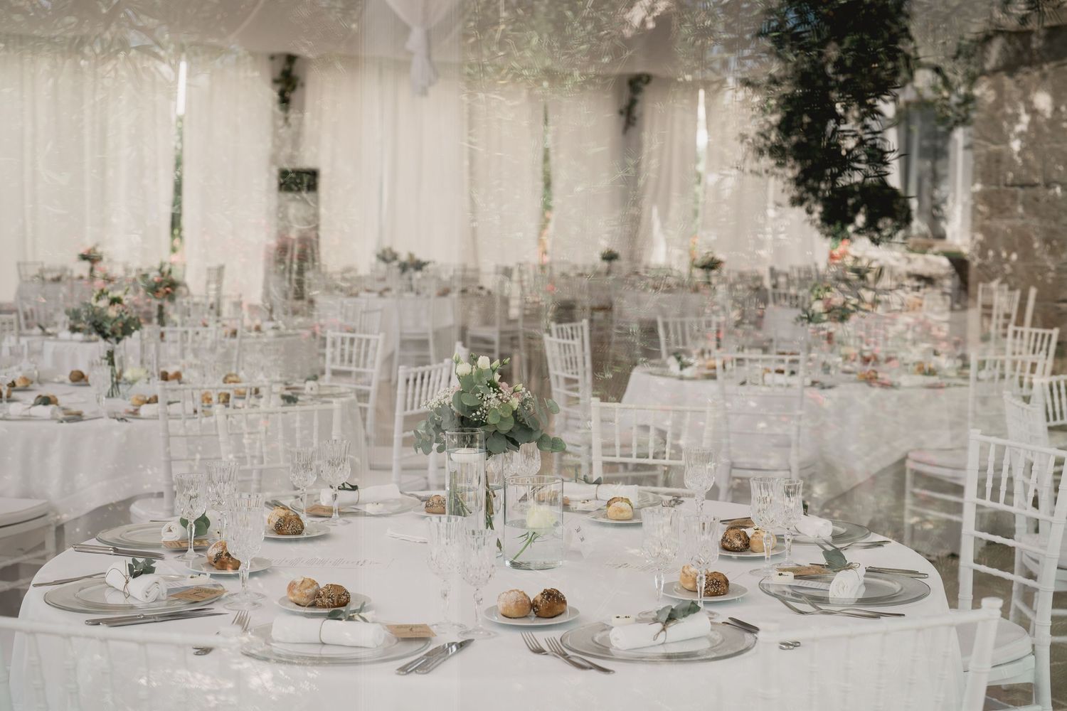 An elegant wedding reception setup with white decor, floral centerpieces and chiavari chairs.