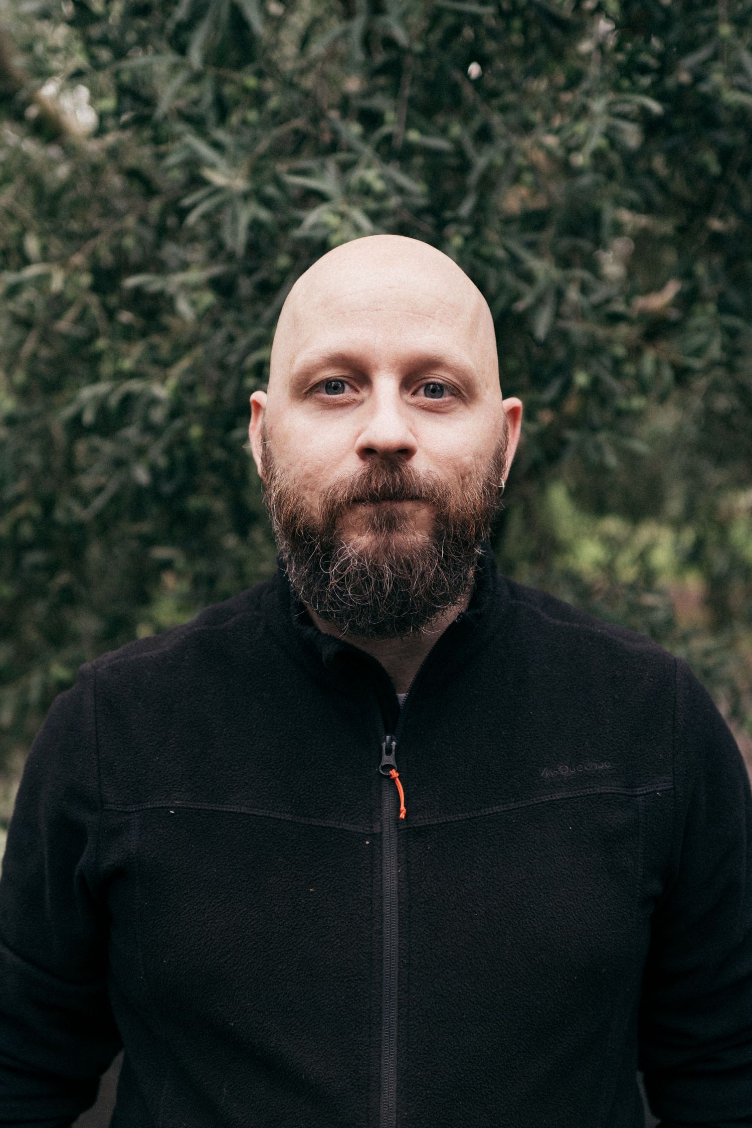 Portrait of person wearing black fleece jacket standing in front of leafy trees.