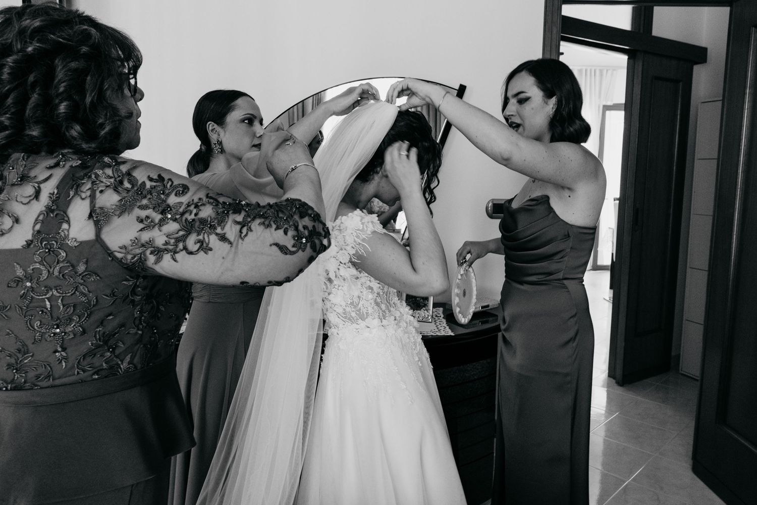 Black and white image of a wedding preparation moment with attendants adjusting the veil.