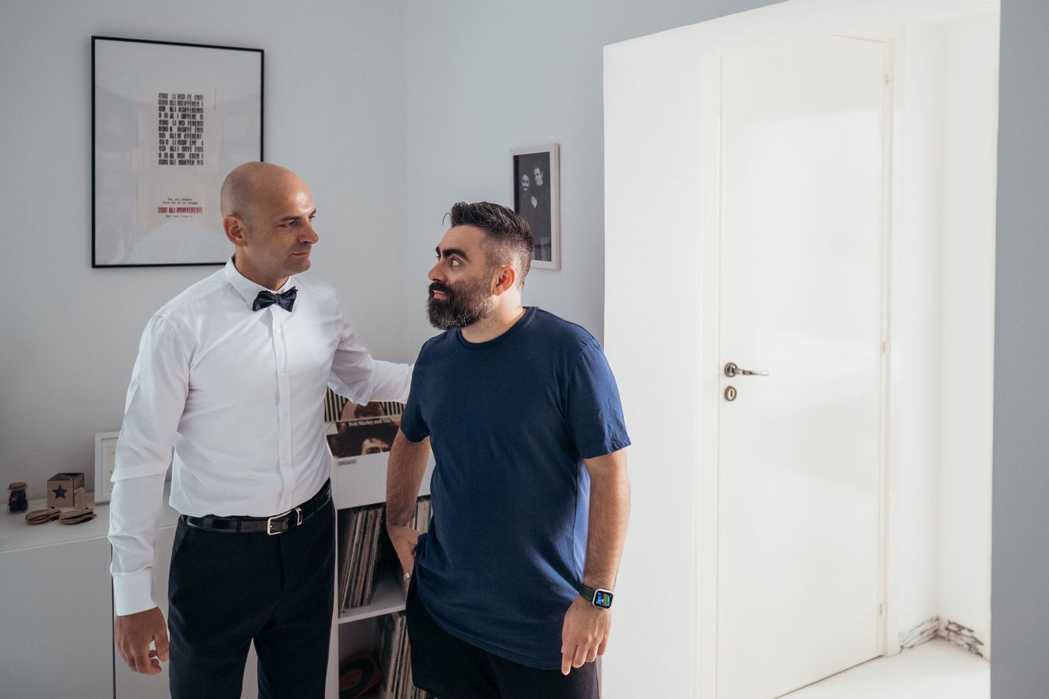 Two people converse in a white room with minimal decor.