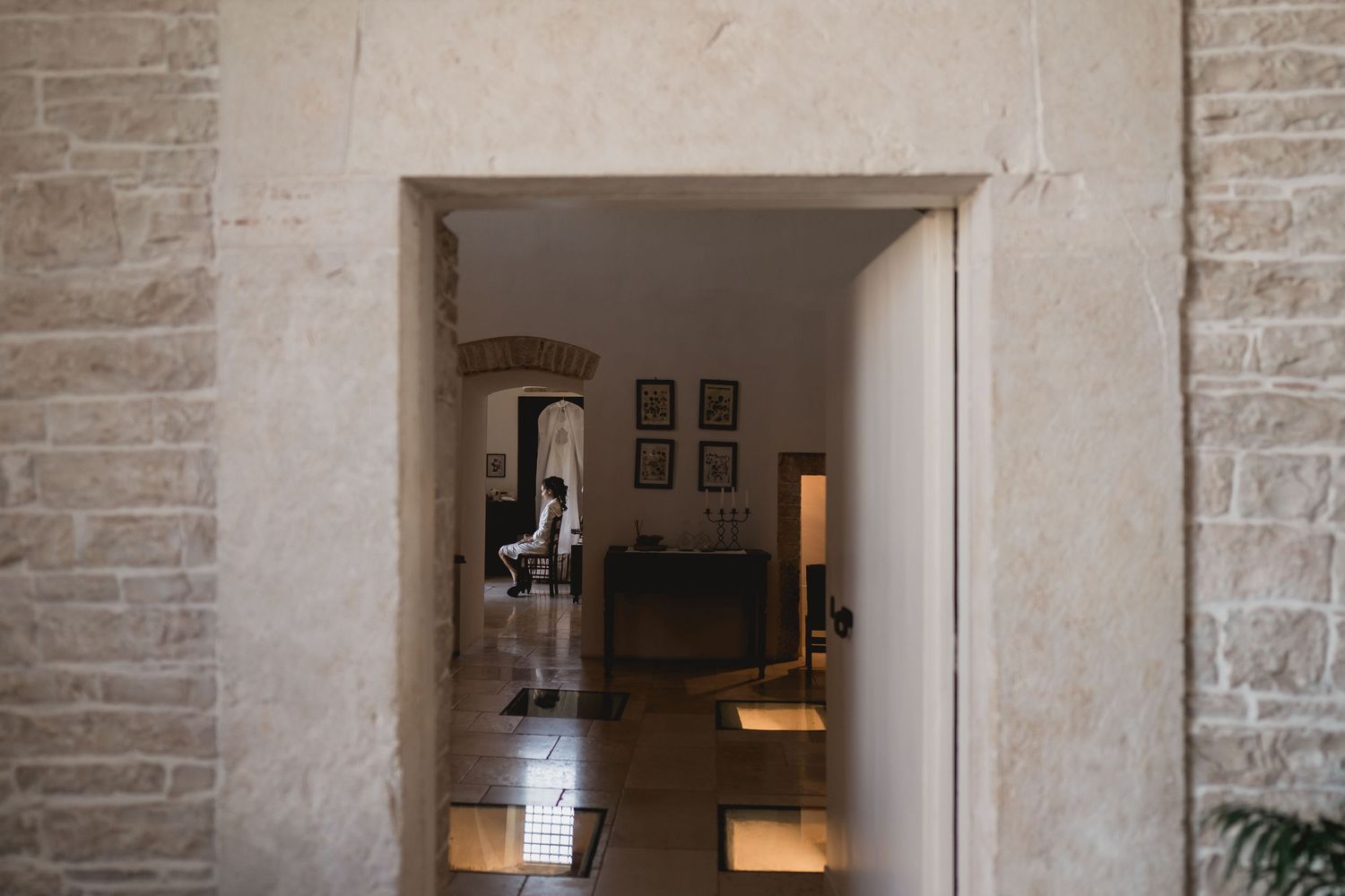 A glimpse through a stone archway into an elegantly lit hallway with framed artwork.