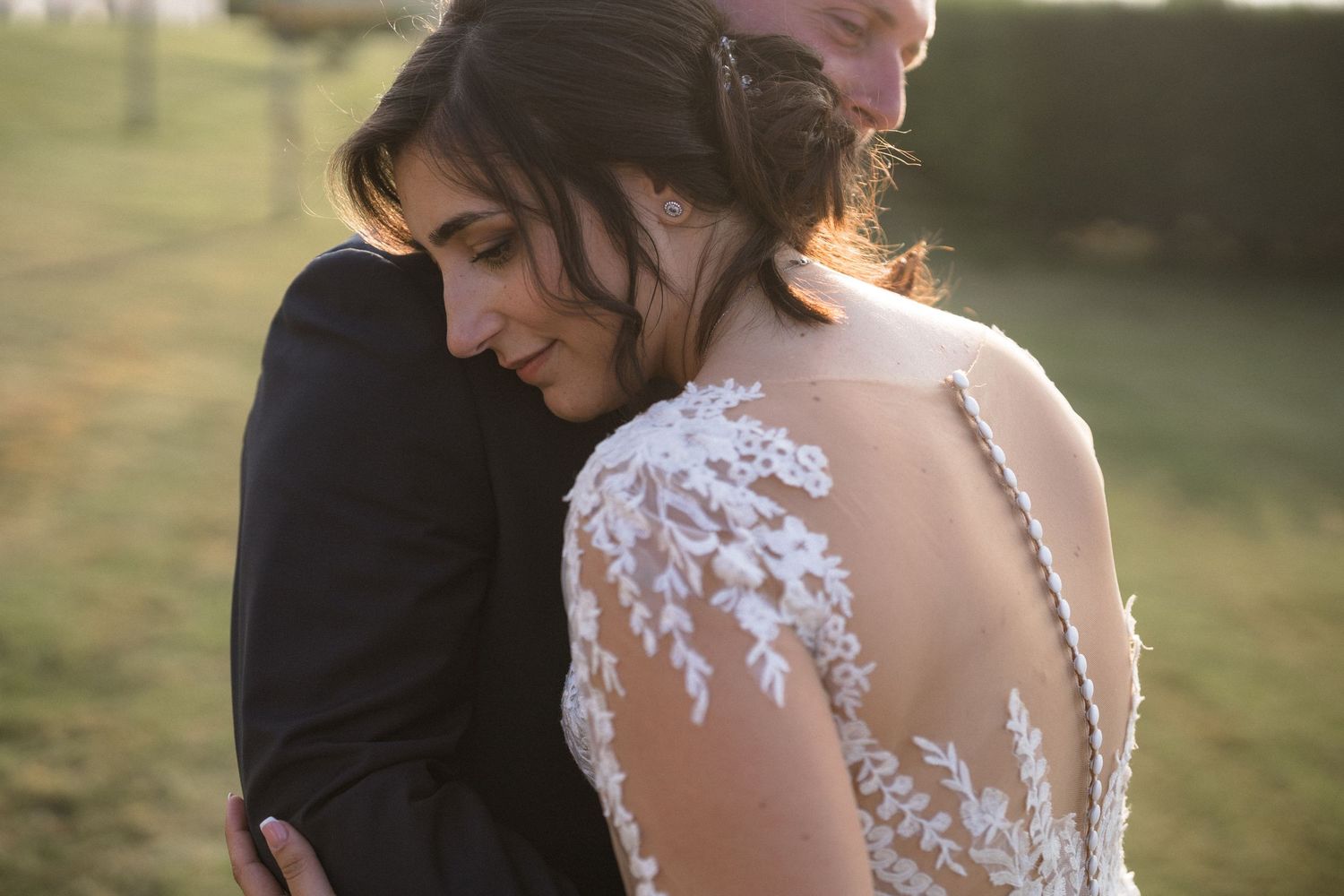 Wedding couple embracing in golden sunlight with detailed lace dress visible.