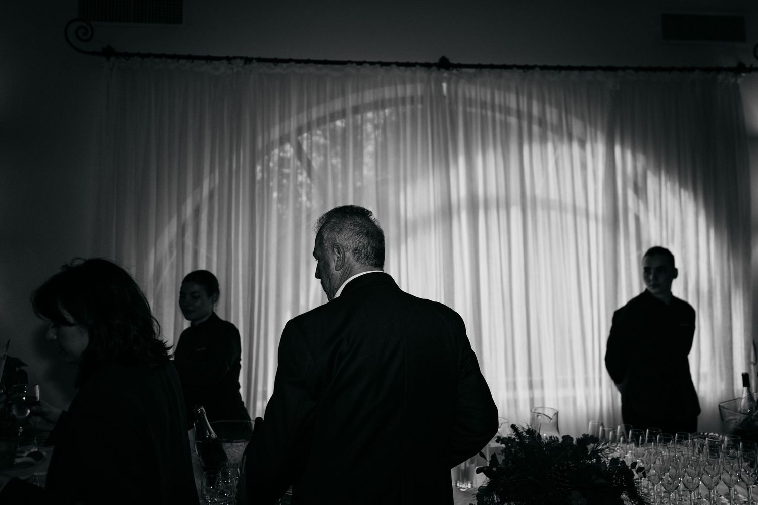 Elegant black and white photo of wedding reception guests silhouetted against draped white backdrop.