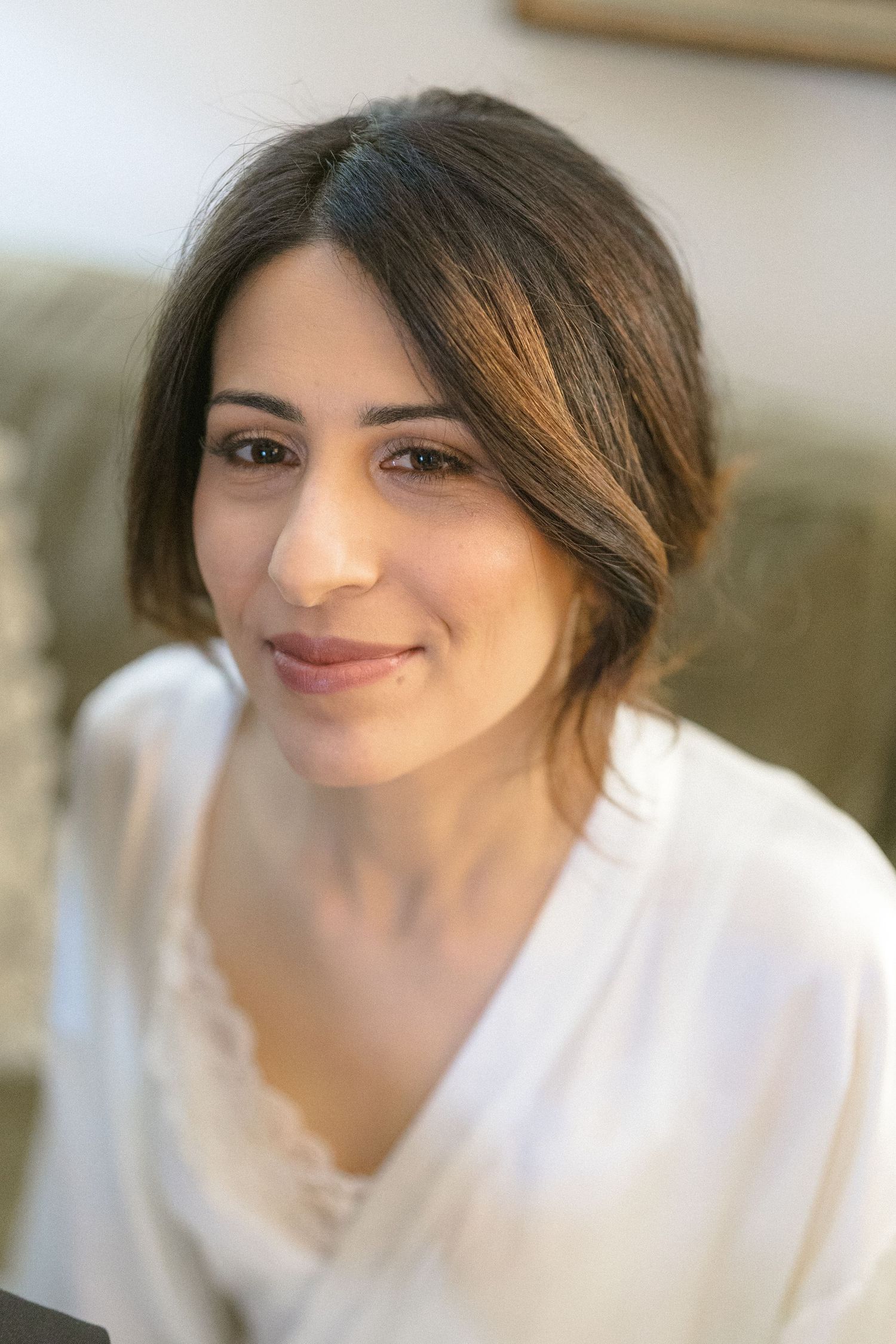 Beautiful dark-haired bride smiling softly in a white robe during wedding preparations.