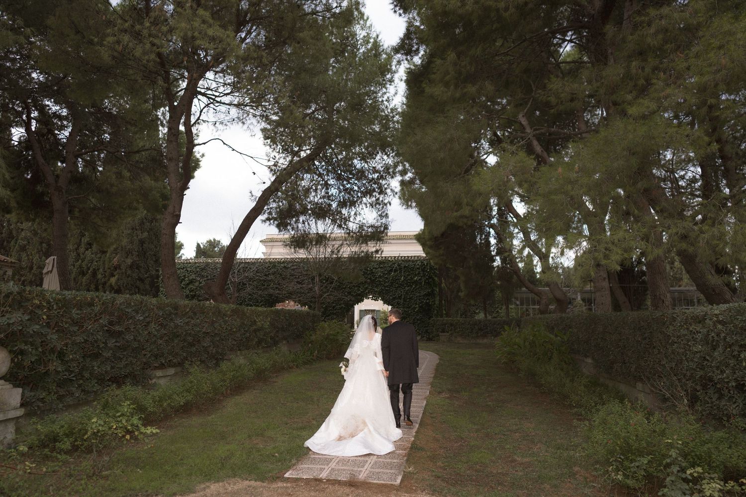 Bride and groom walking hand in hand through a lush garden pathway after their wedding ceremony.