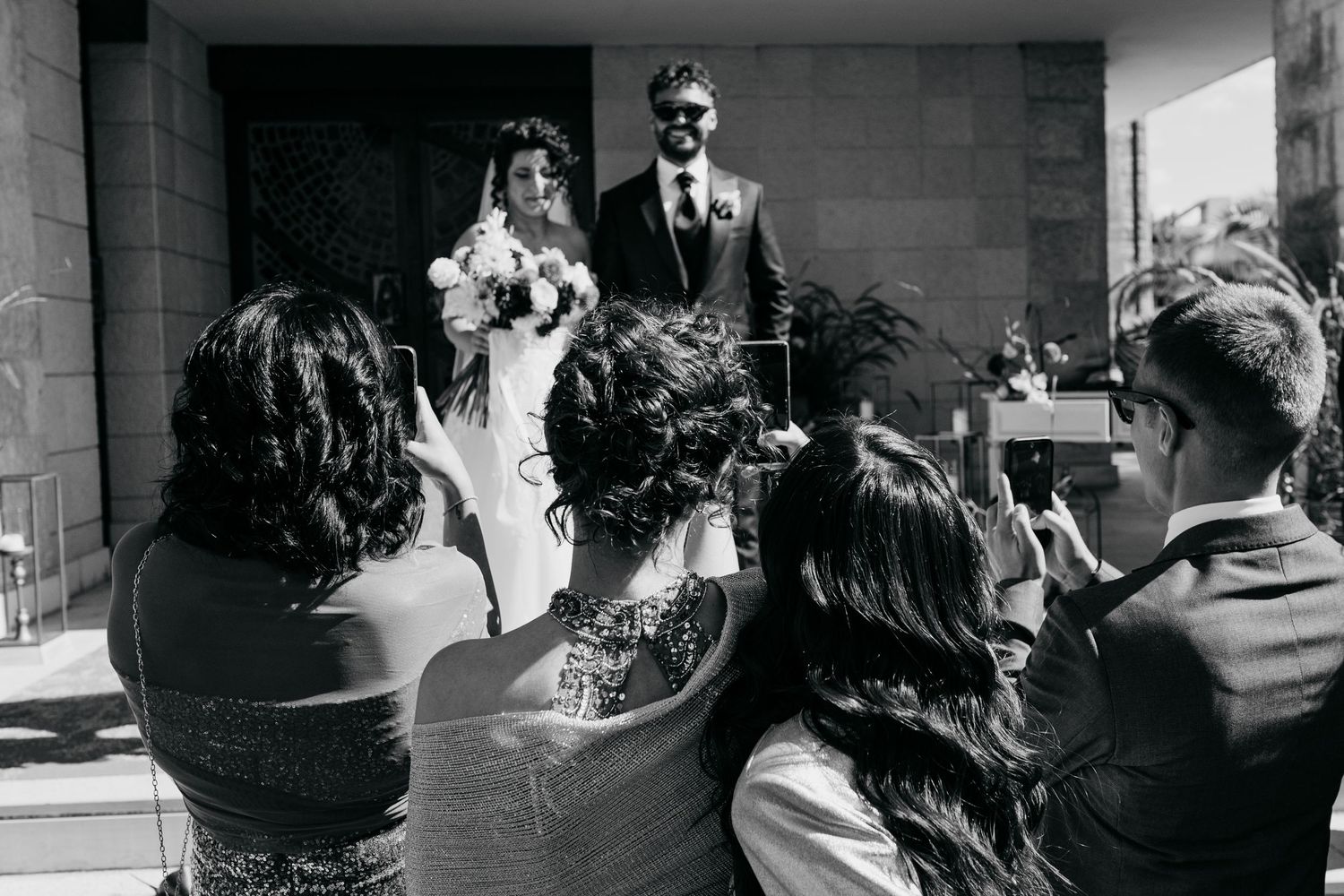 Guests photograph a bride and groom standing at the entrance of a church after their wedding ceremony.