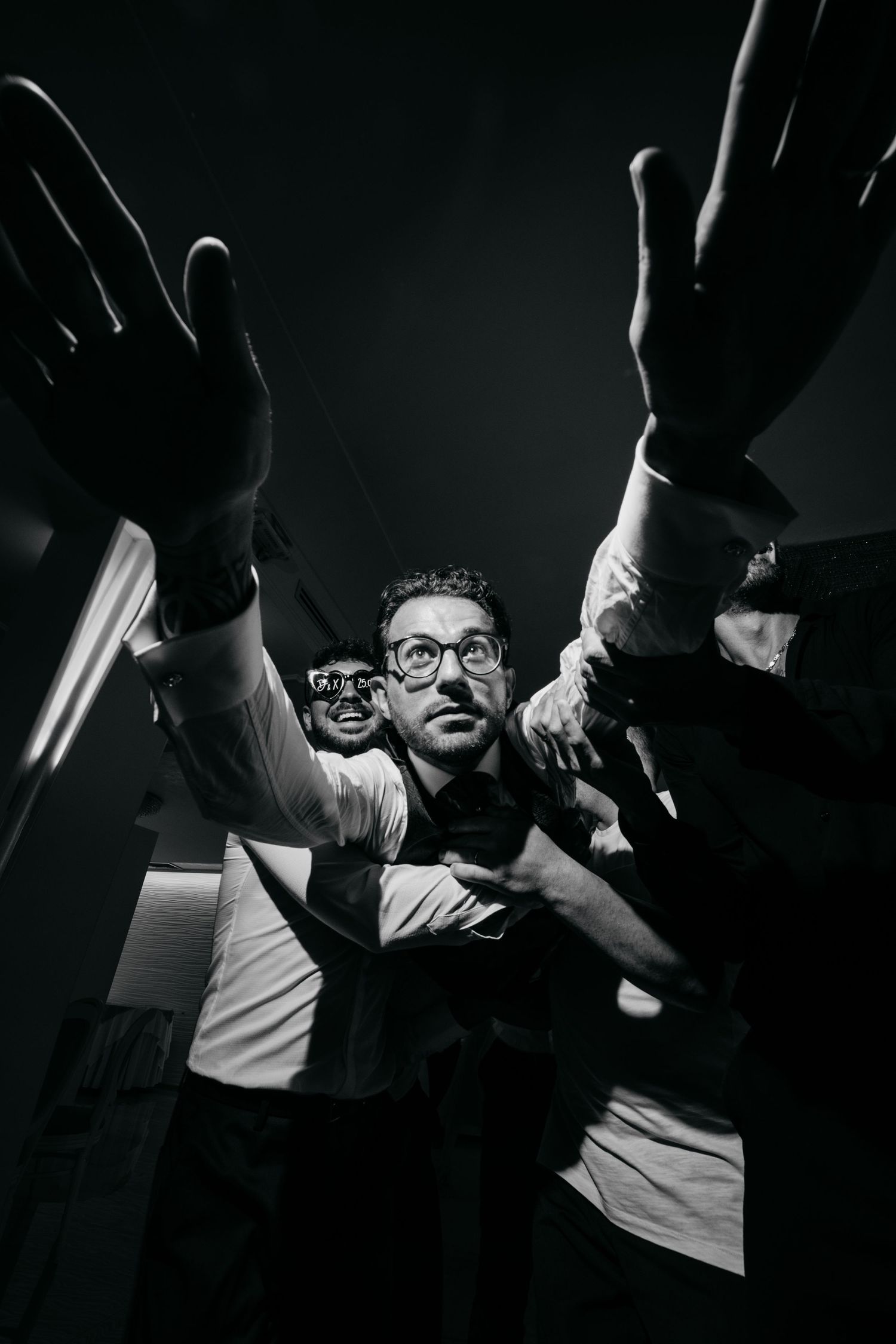 Dramatic black and white photo of wedding guests with raised hands.