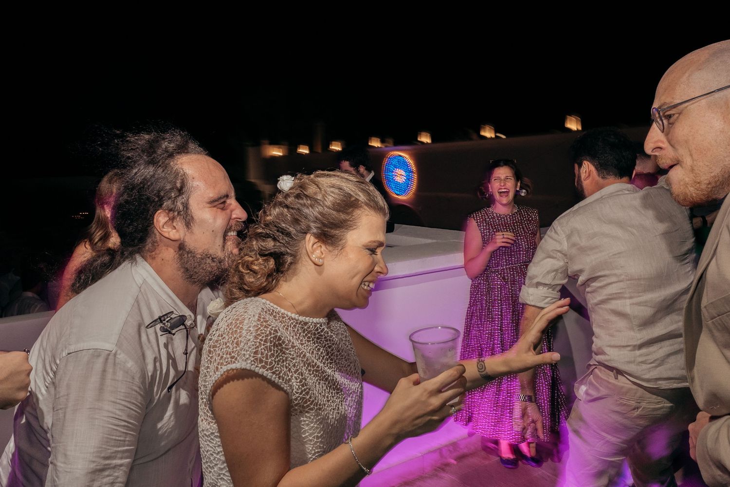 Wedding guests dancing enthusiastically under colorful lighting at an evening celebration.