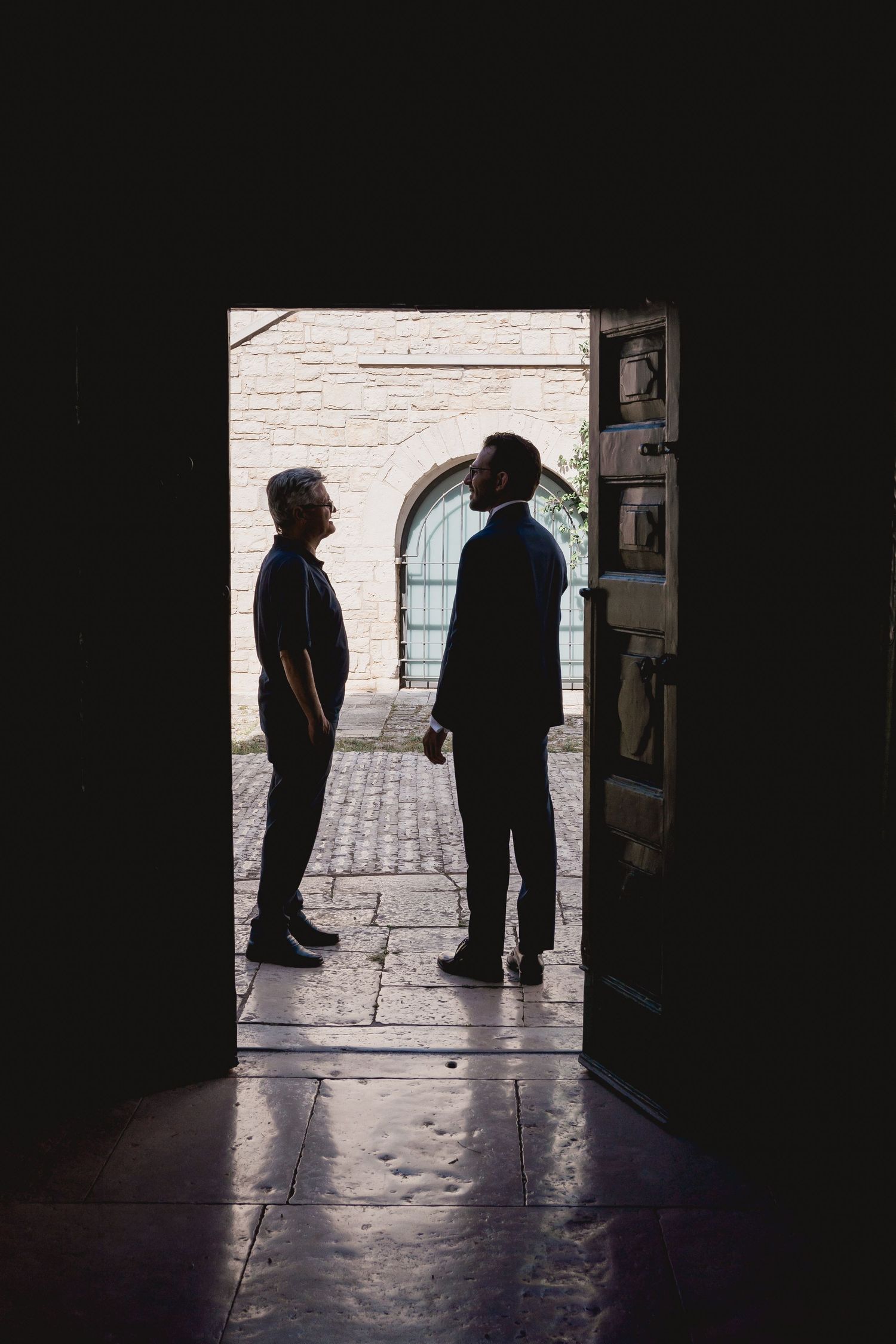 Dramatic silhouette of two figures standing in a stone archway.