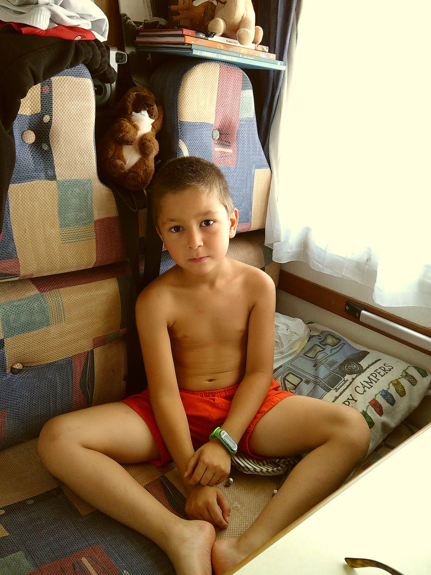 Young person sitting by window with stuffed animals and patchwork quilt visible on shelves.