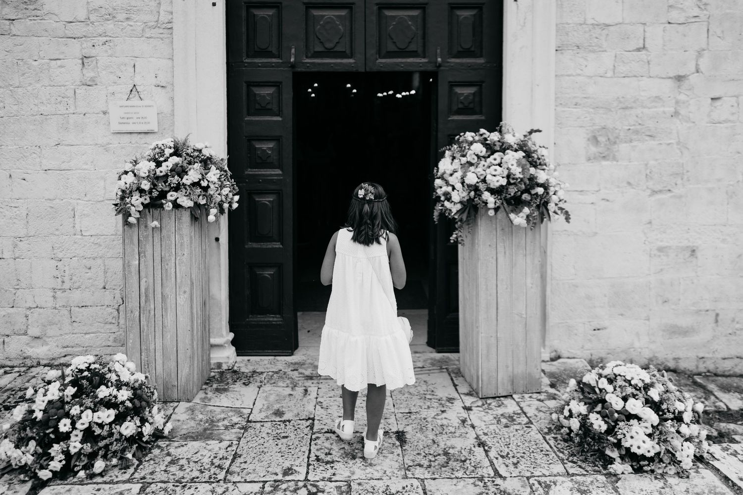 Exterior view of a white stone building with black doors and potted plants.