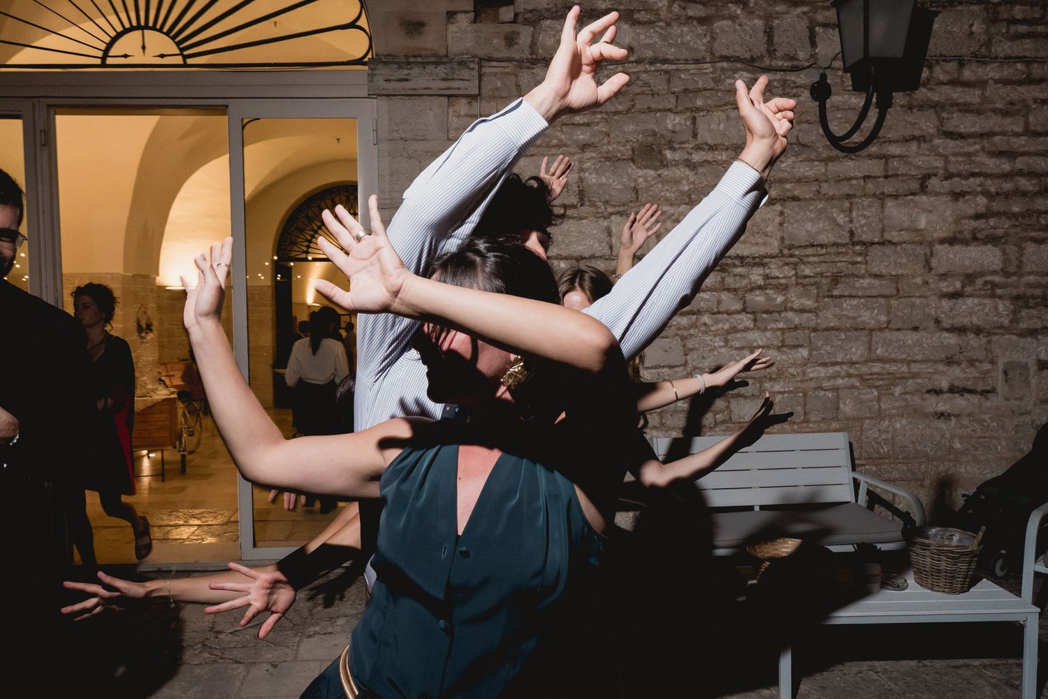 Wedding guests dancing energetically with raised arms at an indoor reception venue with stone walls.