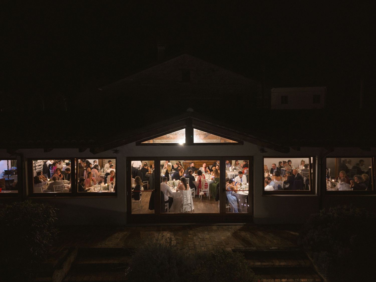 Dark reception hall with illuminated windows and guests visible through glass panes at night.