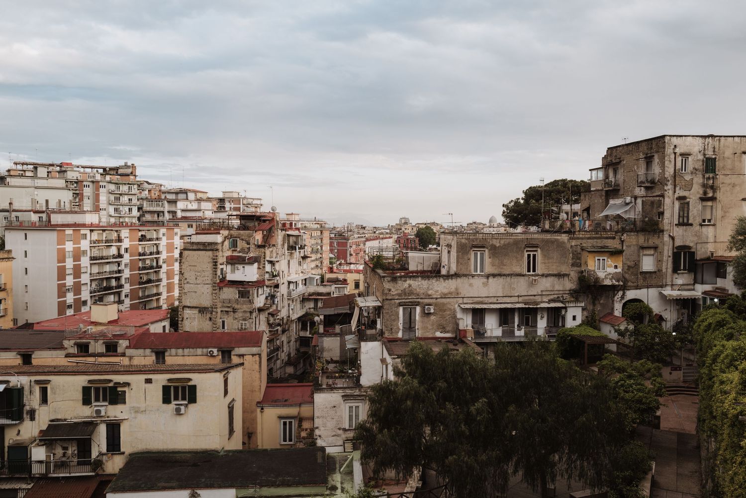 View of residential apartment buildings on hillside in Naples, Italy with overcast sky and lush greenery.