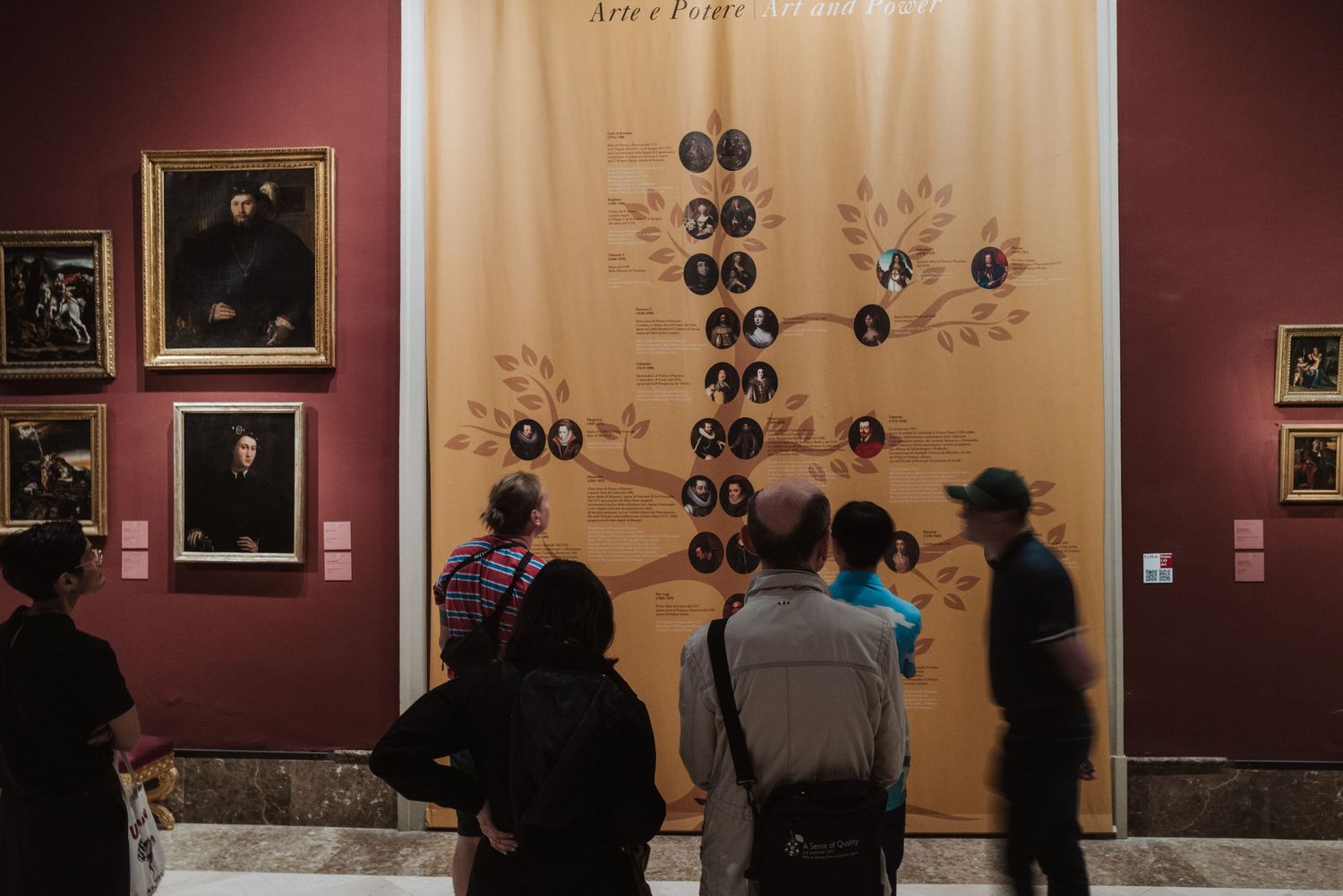 Museum visitors examining a historical family tree or genealogical display on a gallery wall.