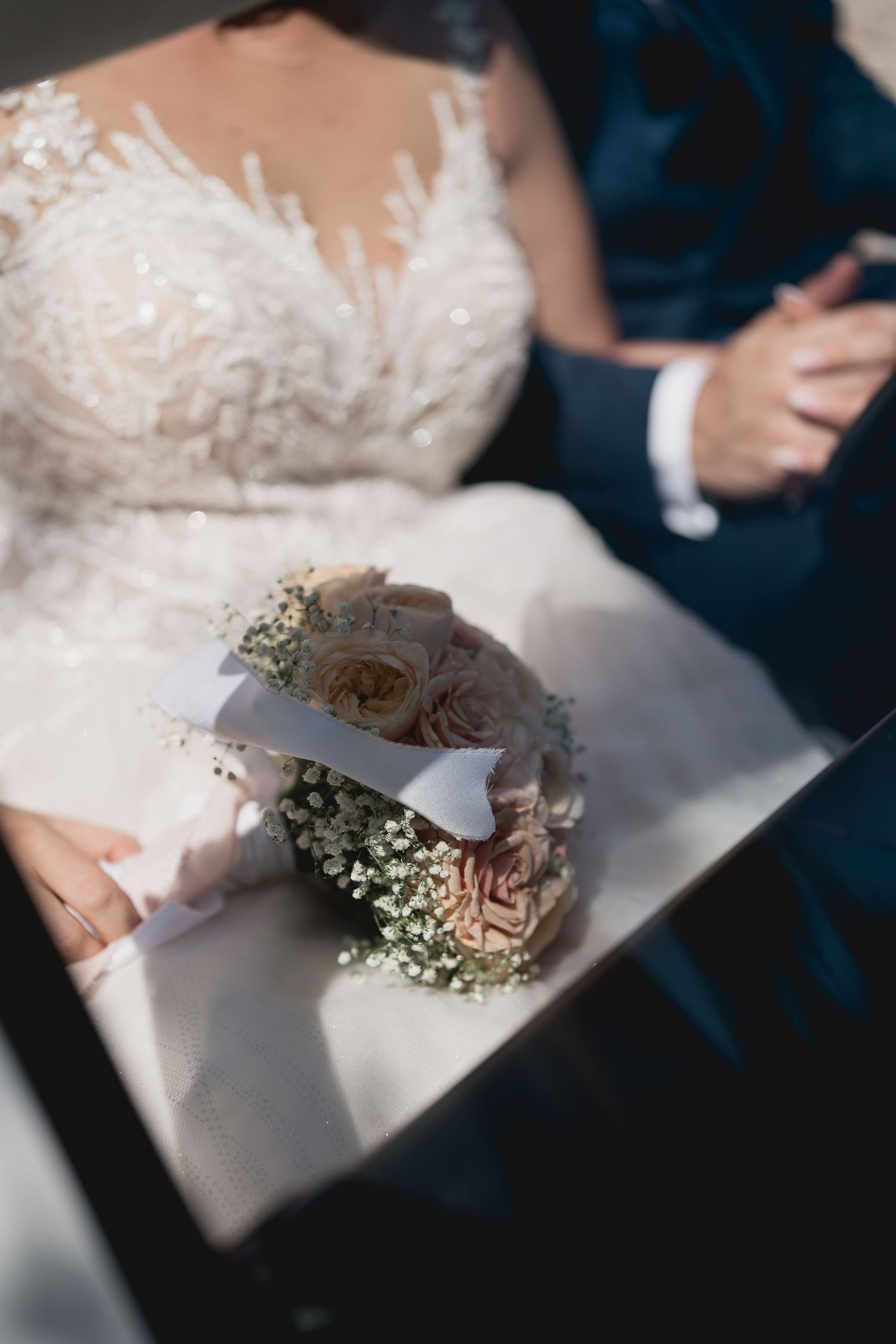 Detail shot of a bridal bouquet with baby's breath and roses on a white wedding dress.