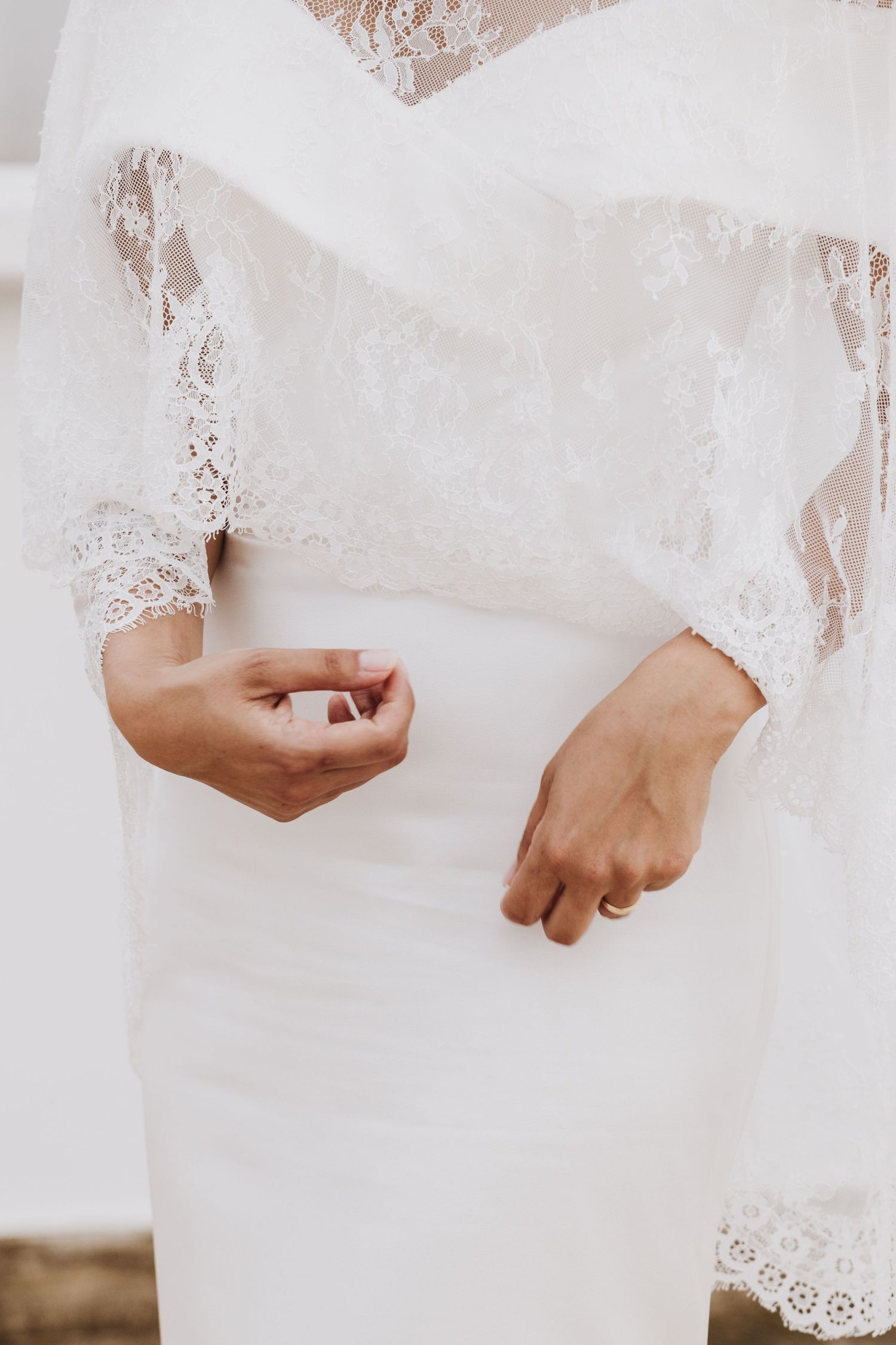 Detail shot of bride's hands against white lace wedding dress.