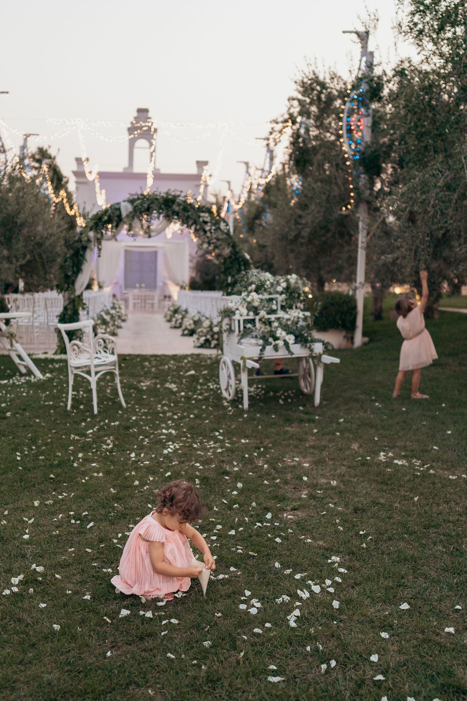 A dreamy wedding venue with white chairs, floral arrangements and twinkling lights at dusk.