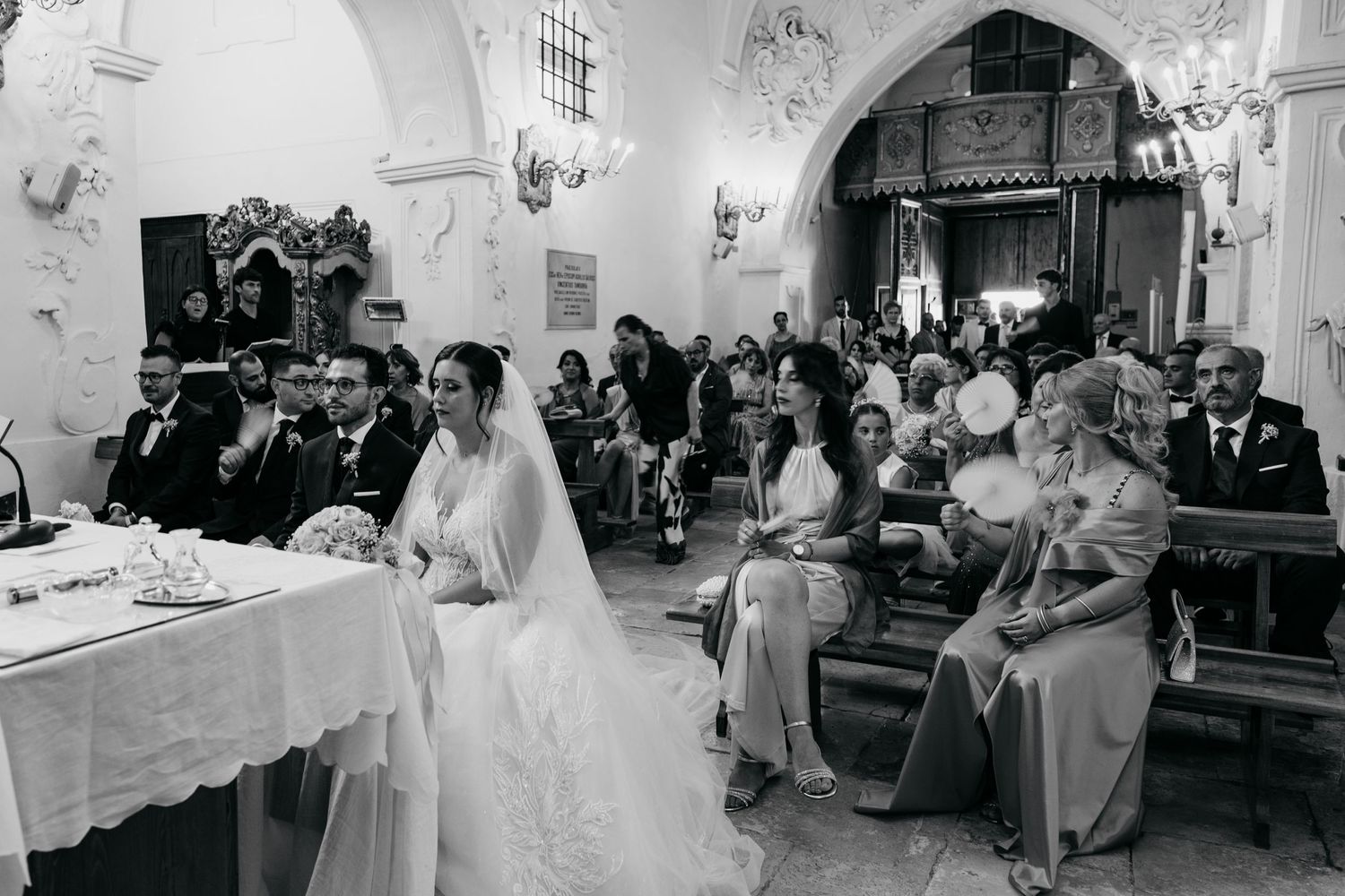 A black and white photograph capturing a traditional church wedding ceremony with gathered guests.