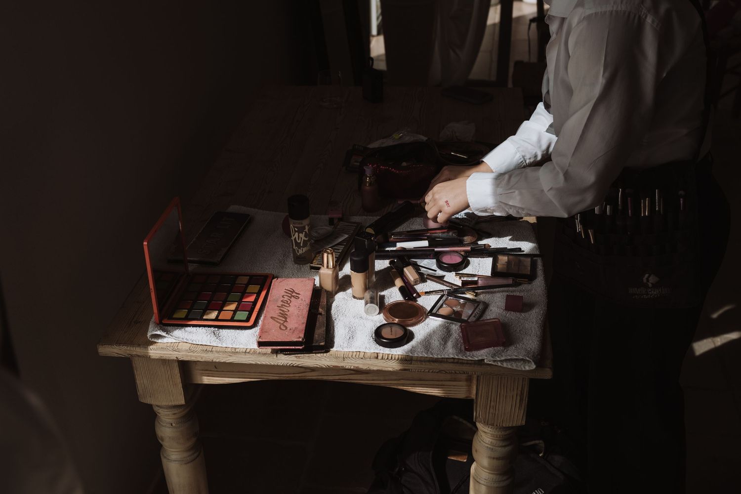 Hands preparing drinks at a dimly lit wooden table with various bottles and equipment.
