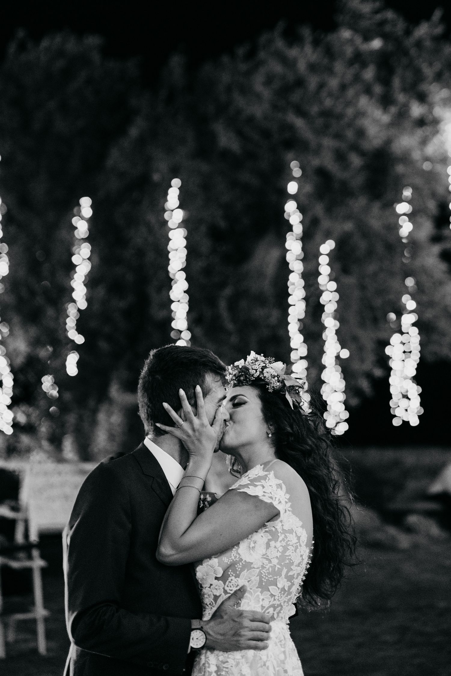 A romantic black and white photo sequence of newlyweds sharing a kiss with string lights twinkling in the background.