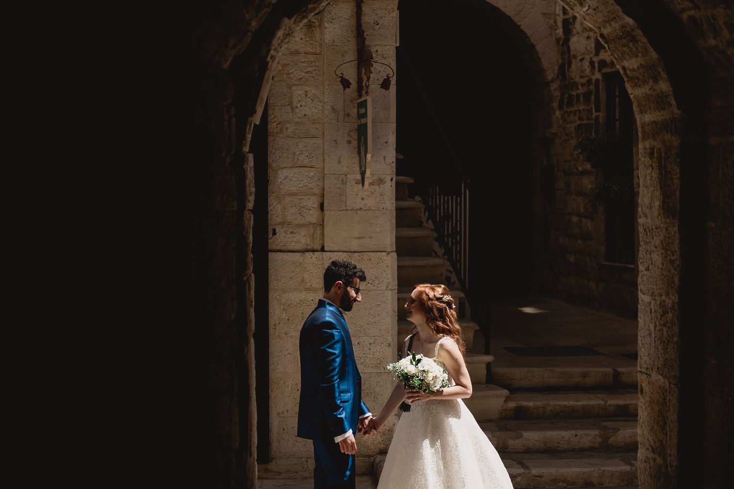 Wedding couple standing in dramatic stone archway with natural lighting.