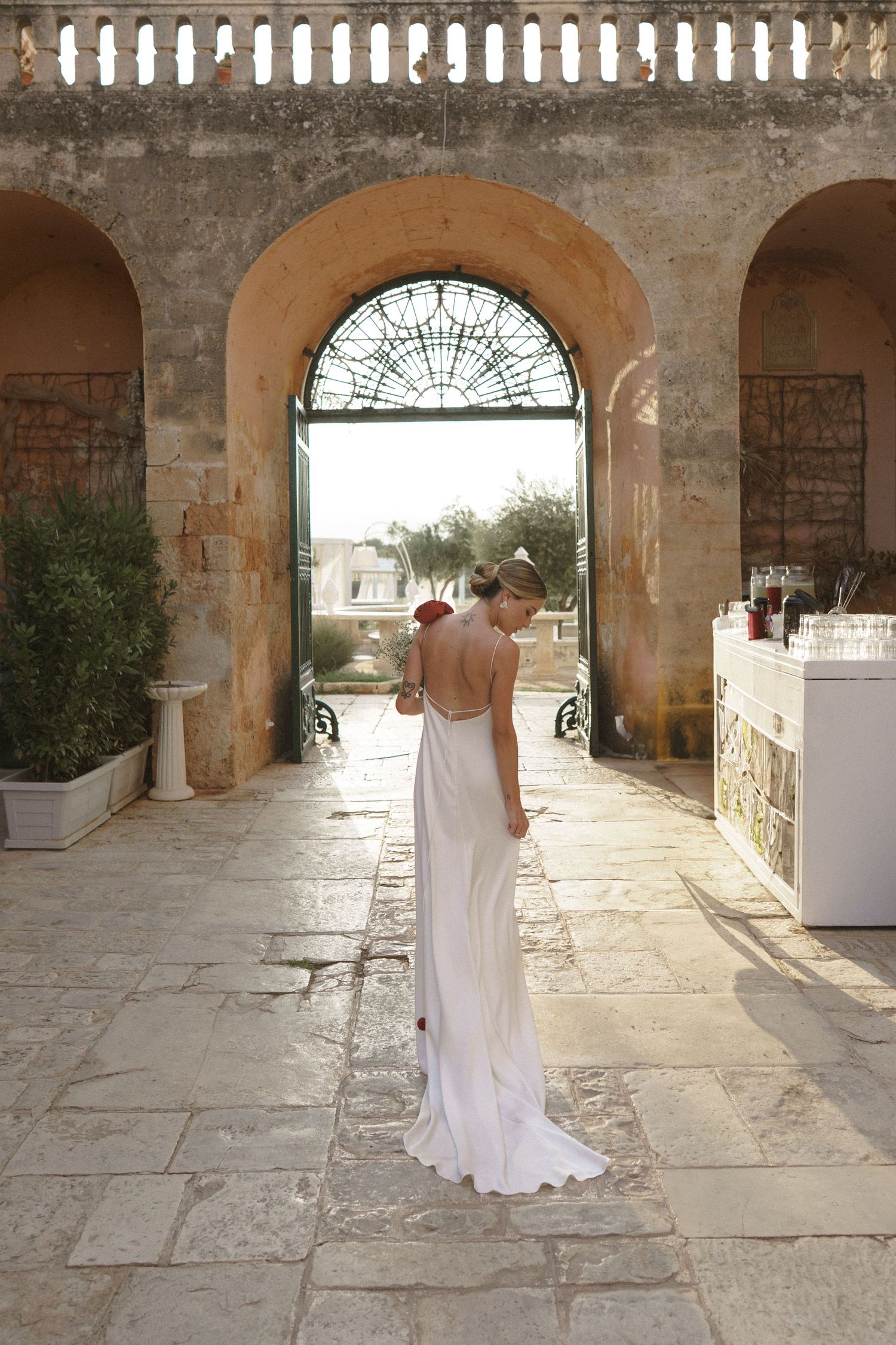 A flowing white wedding gown is captured in an elegant archway with stone walls and decorative stained glass details.