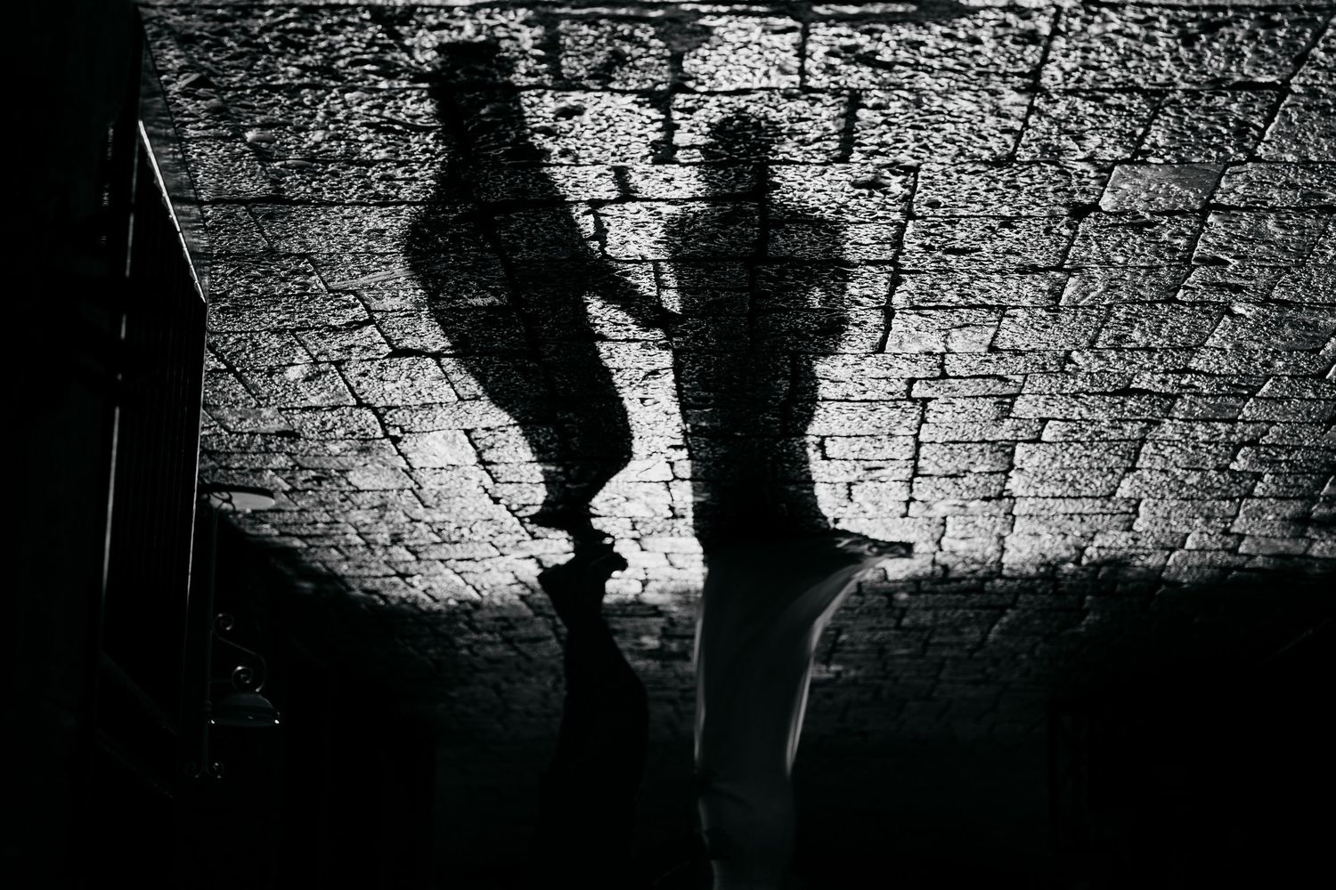 Artistic black and white silhouettes of people dancing against a textured brick wall.