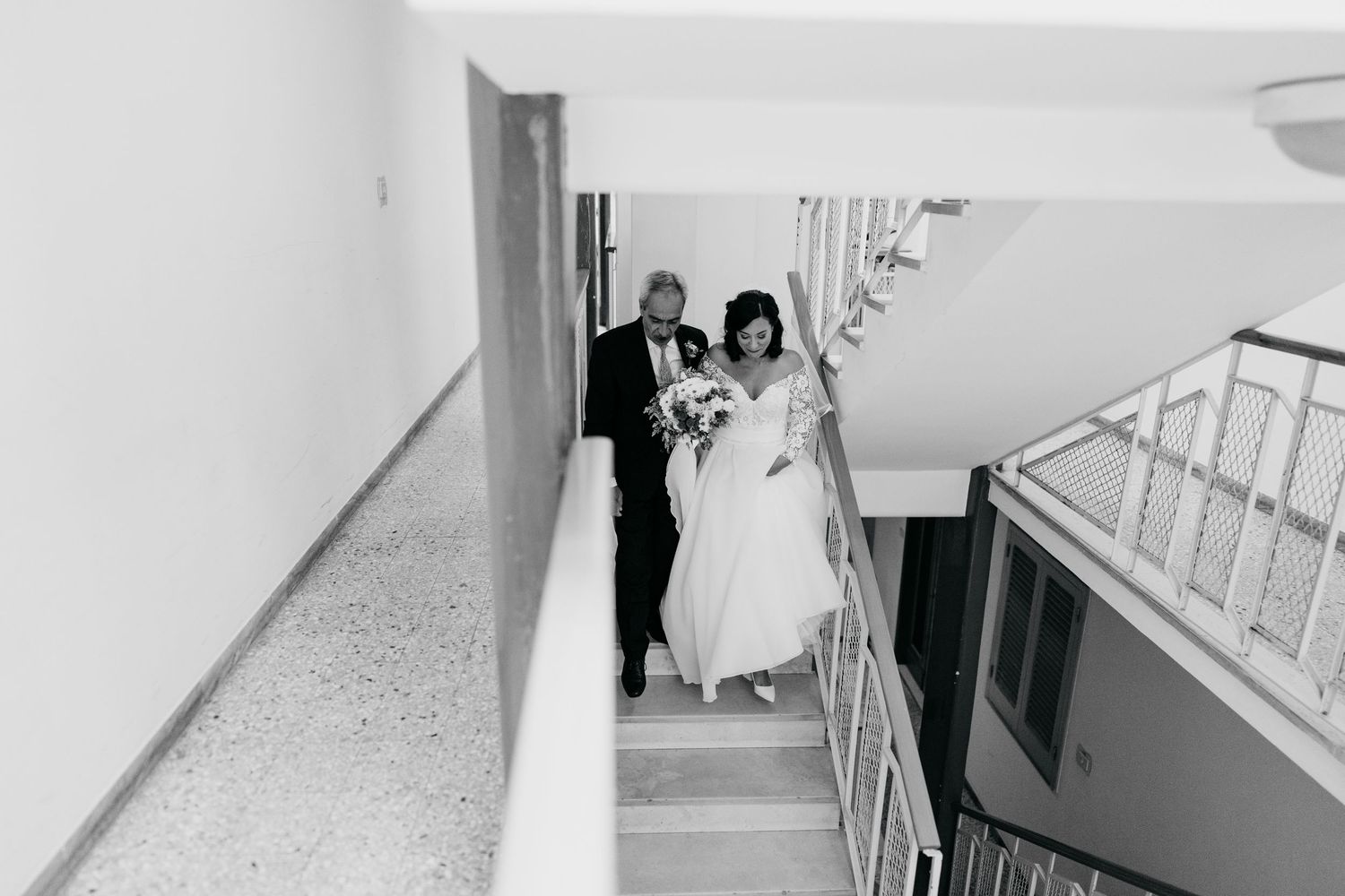 A bride in her wedding dress walks up a bright white staircase on her wedding day.