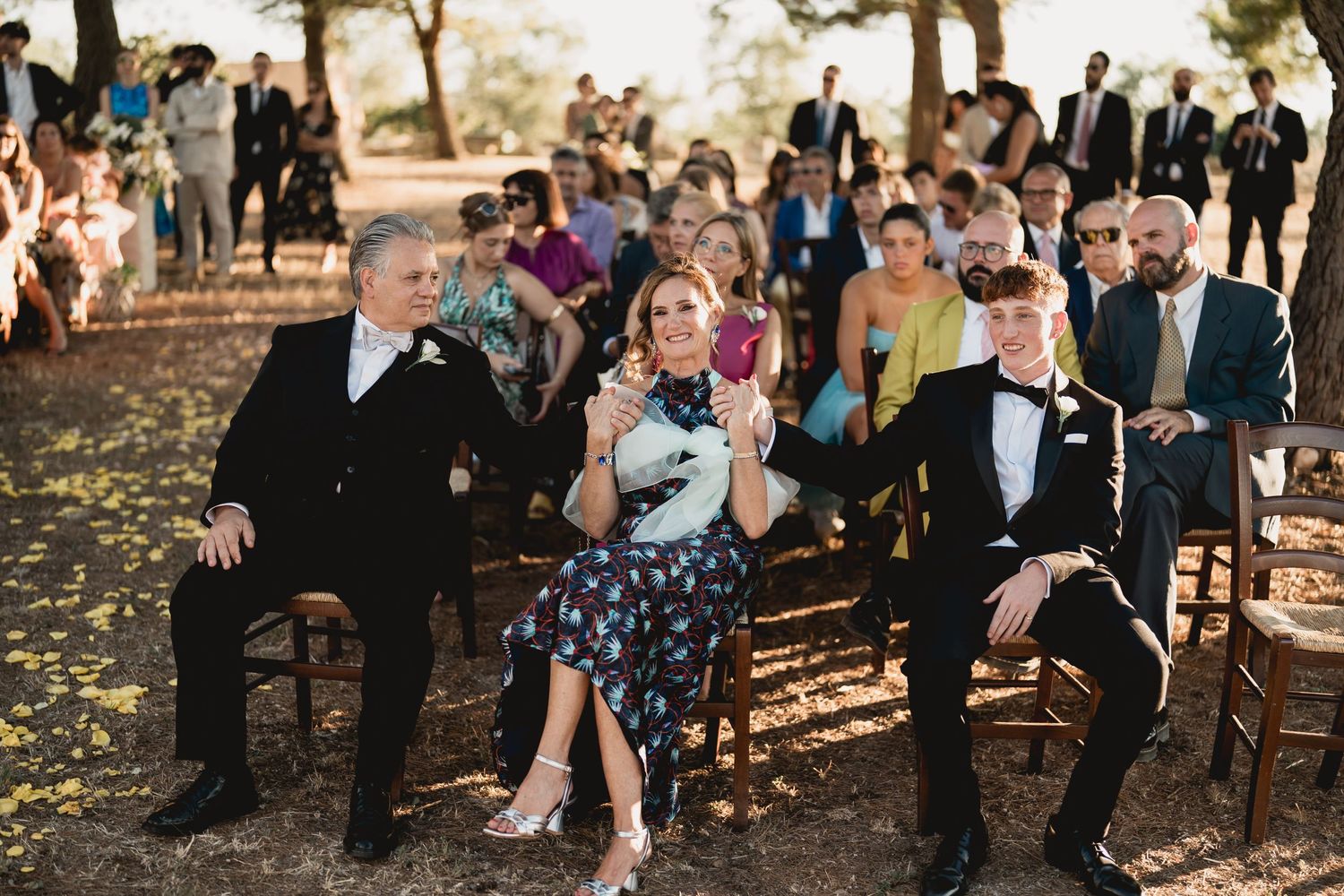 Wedding guests seated on wooden chairs outdoors during an autumn ceremony.