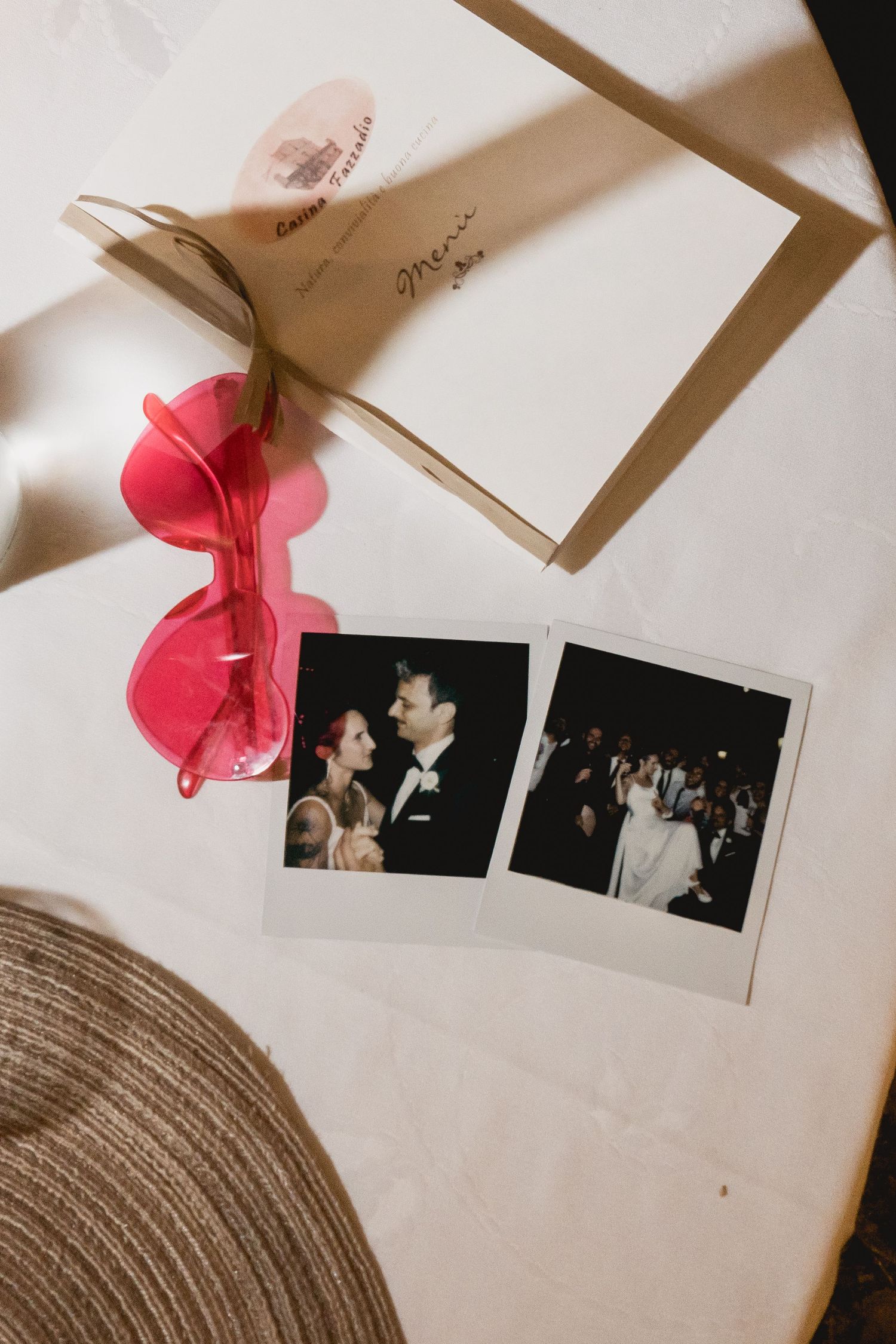 Vintage polaroid photos next to pink heart-shaped sunglasses and brown hat on white surface.