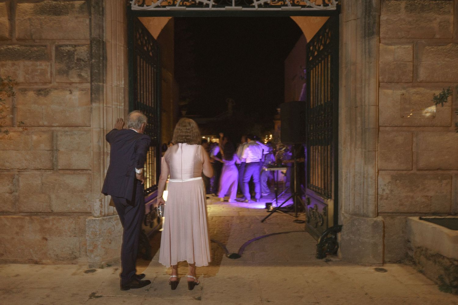Wedding party entering dimly lit stone archway with purple stage lighting visible inside.