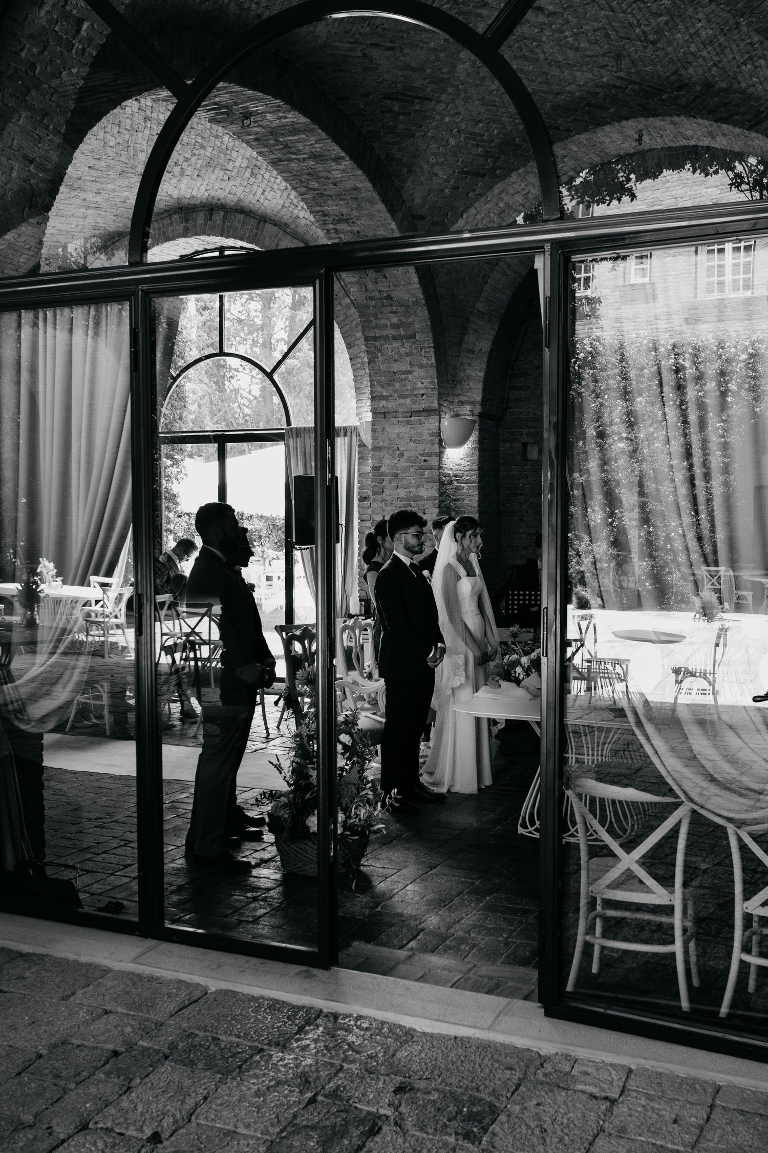 Black and white photo of an arched interior venue space with flowing curtains and natural light.