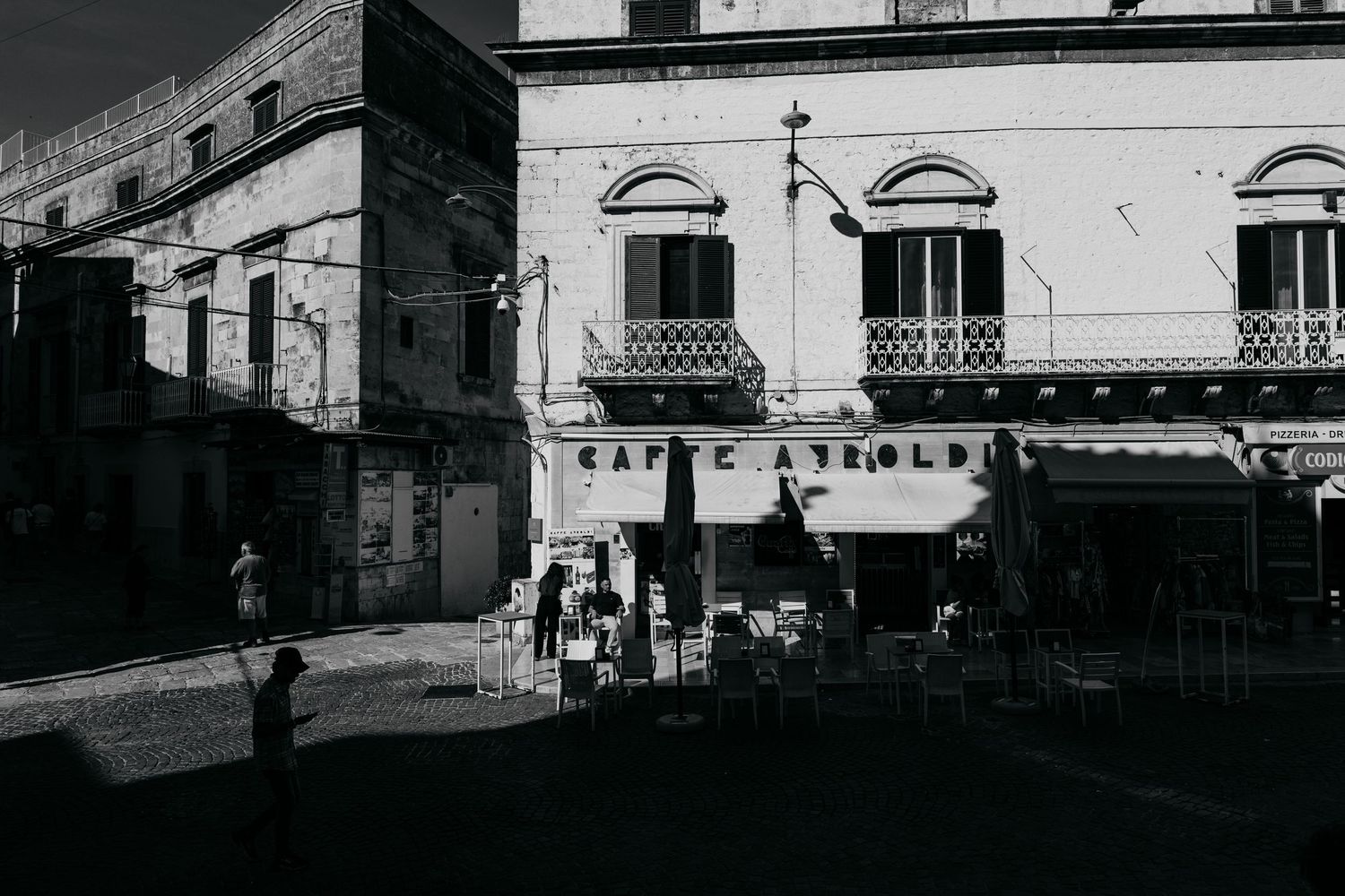 Black and white photo of Caffe Arnoldi exterior in an Italian piazza with people and classic architecture.
