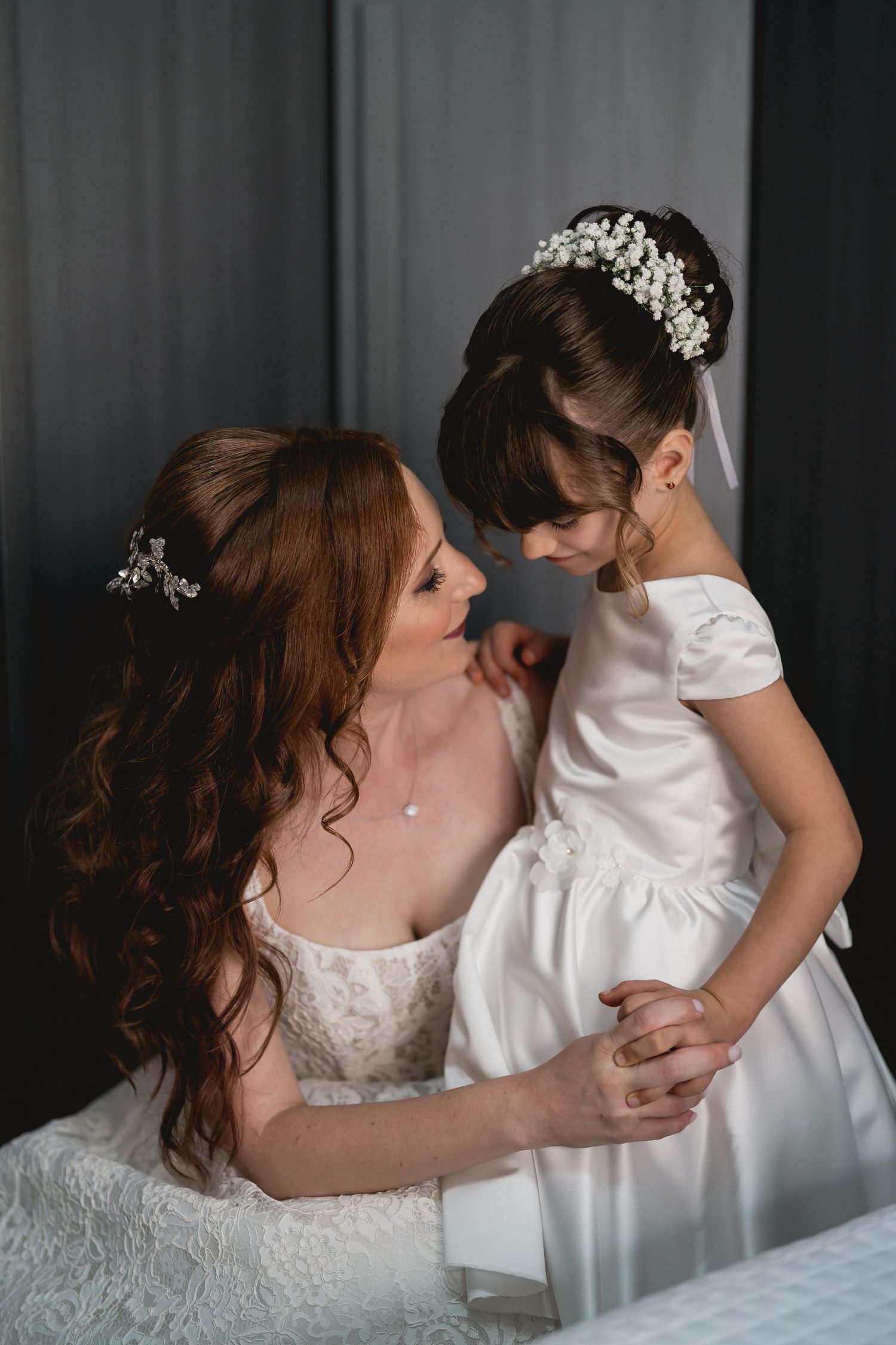 A tender moment captured in black and white as a bride in a white gown embraces a small child in matching white attire.