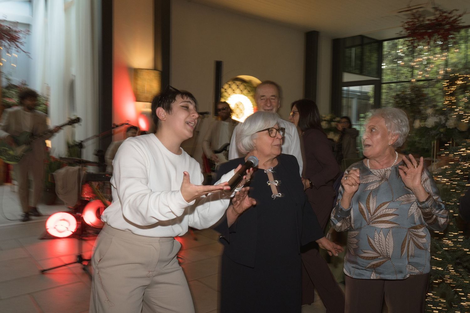 Joyful elderly women dancing and celebrating with confetti at lively indoor wedding reception party.
